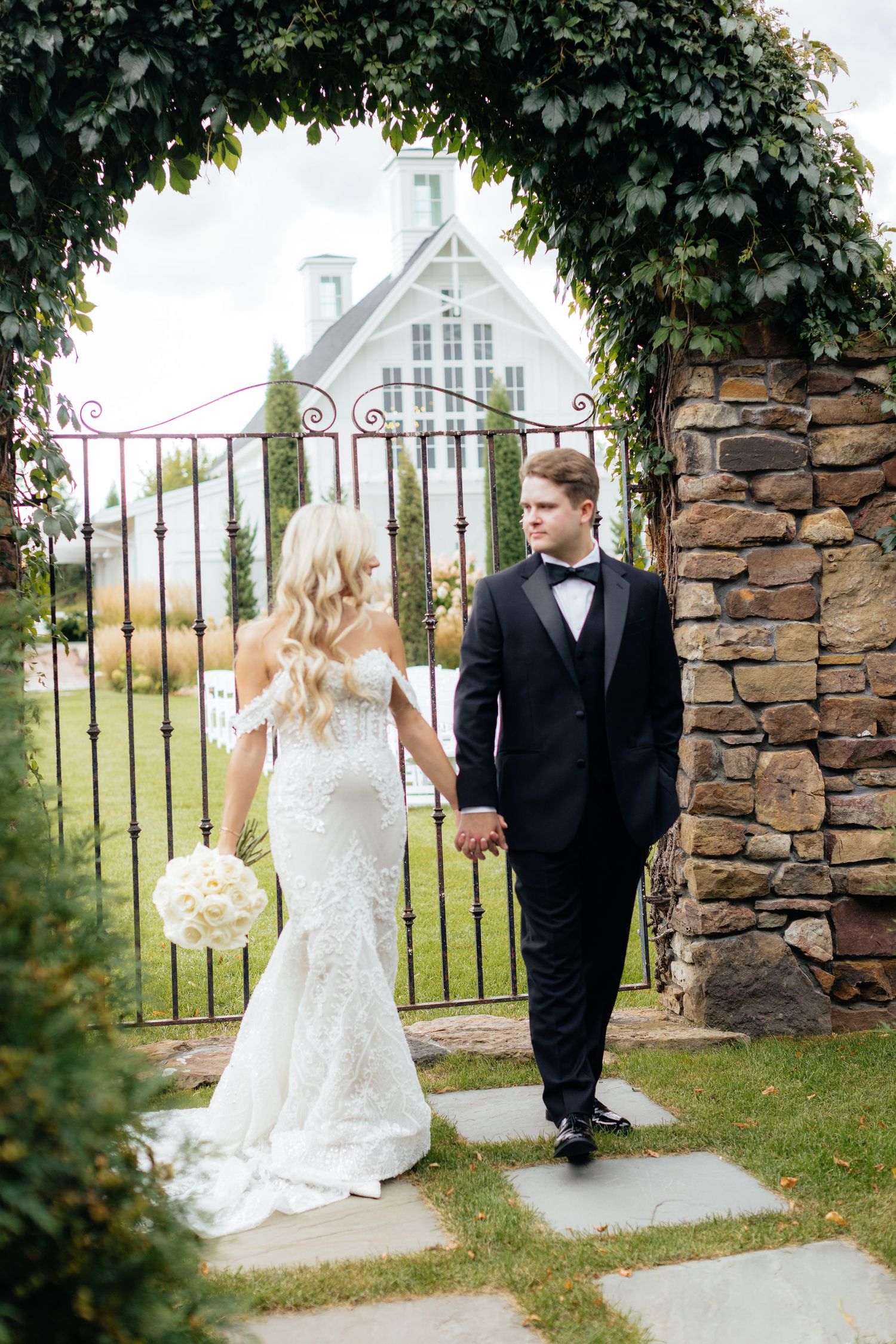 A couple poses under an ivy-covered archway with a white chapel in the background.