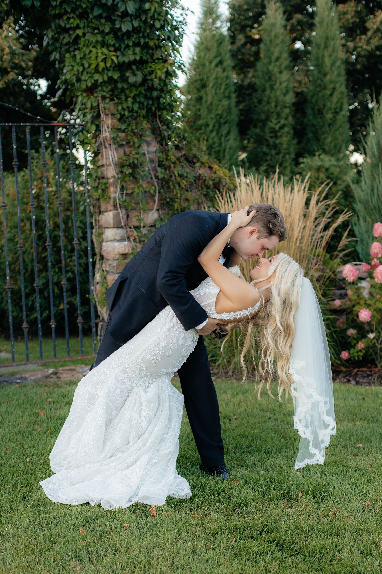 A romantic wedding dip pose sequence photographed outdoors in a garden setting with lush greenery.