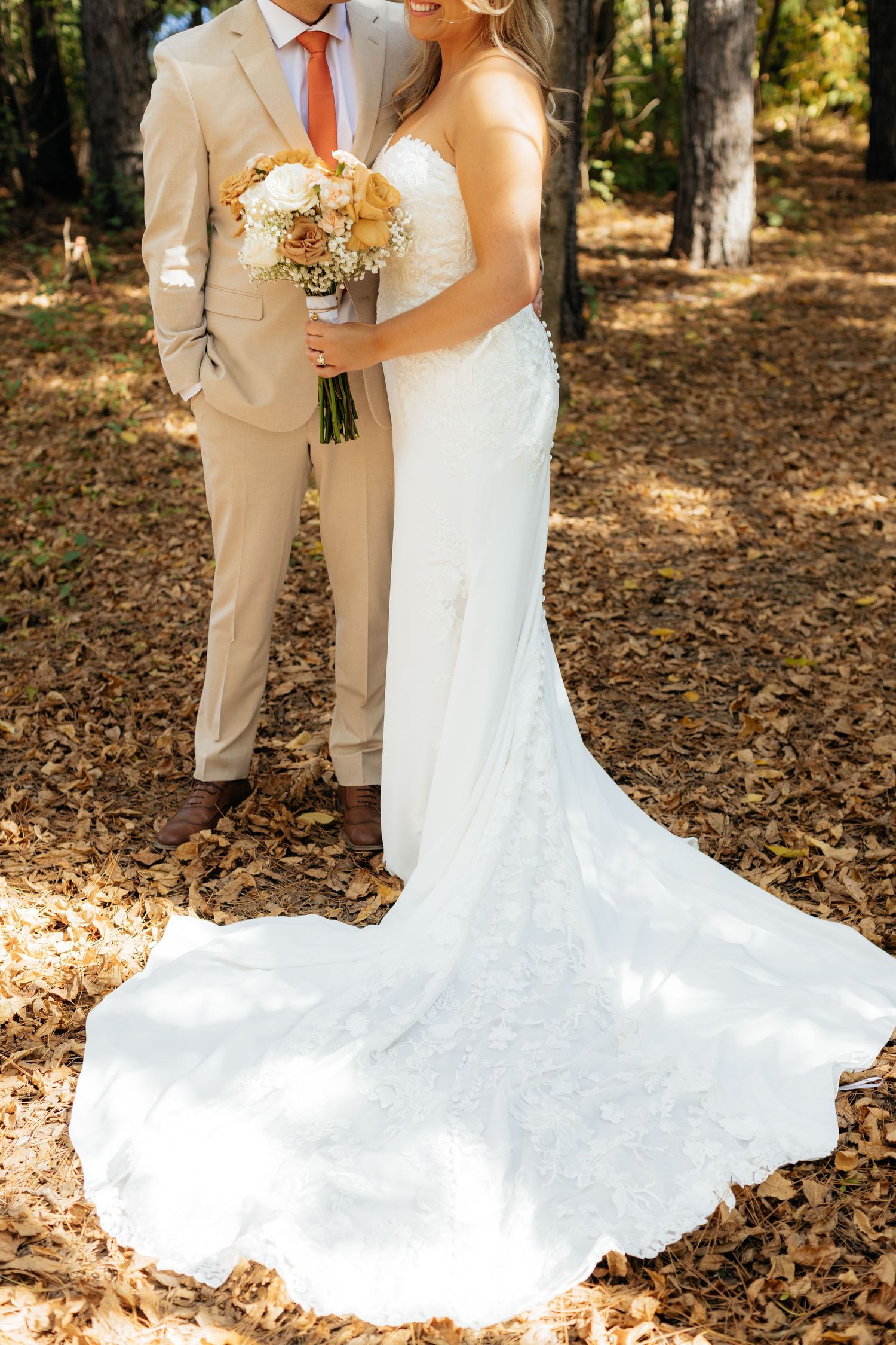 Elegant wedding couple with detailed lace gown and beige suit holding autumn-toned bouquet.