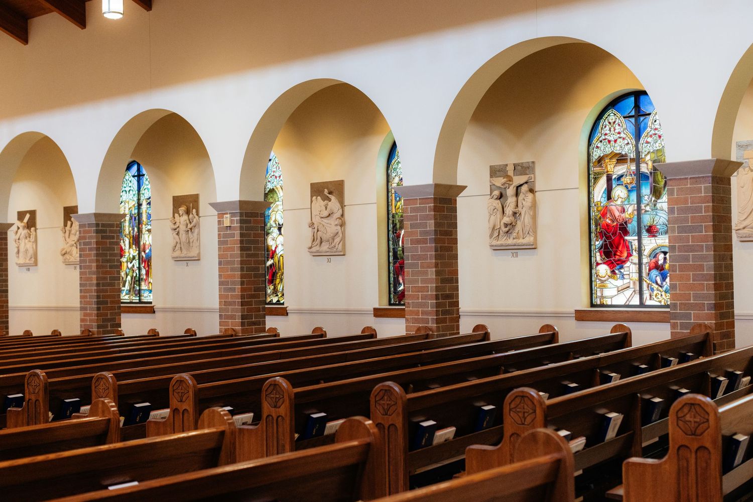 Traditional church interior with wooden pews and arched windows featuring stained glass.