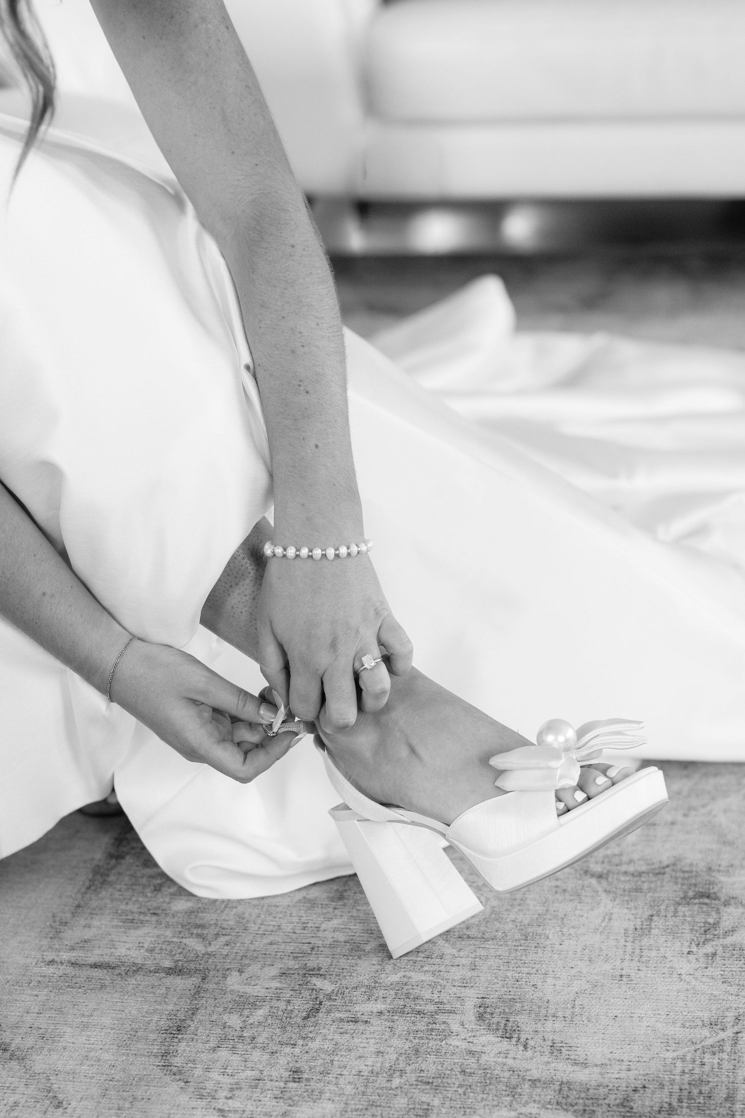 Black and white detail shot of bride putting on wedding shoes with pearl bracelet.