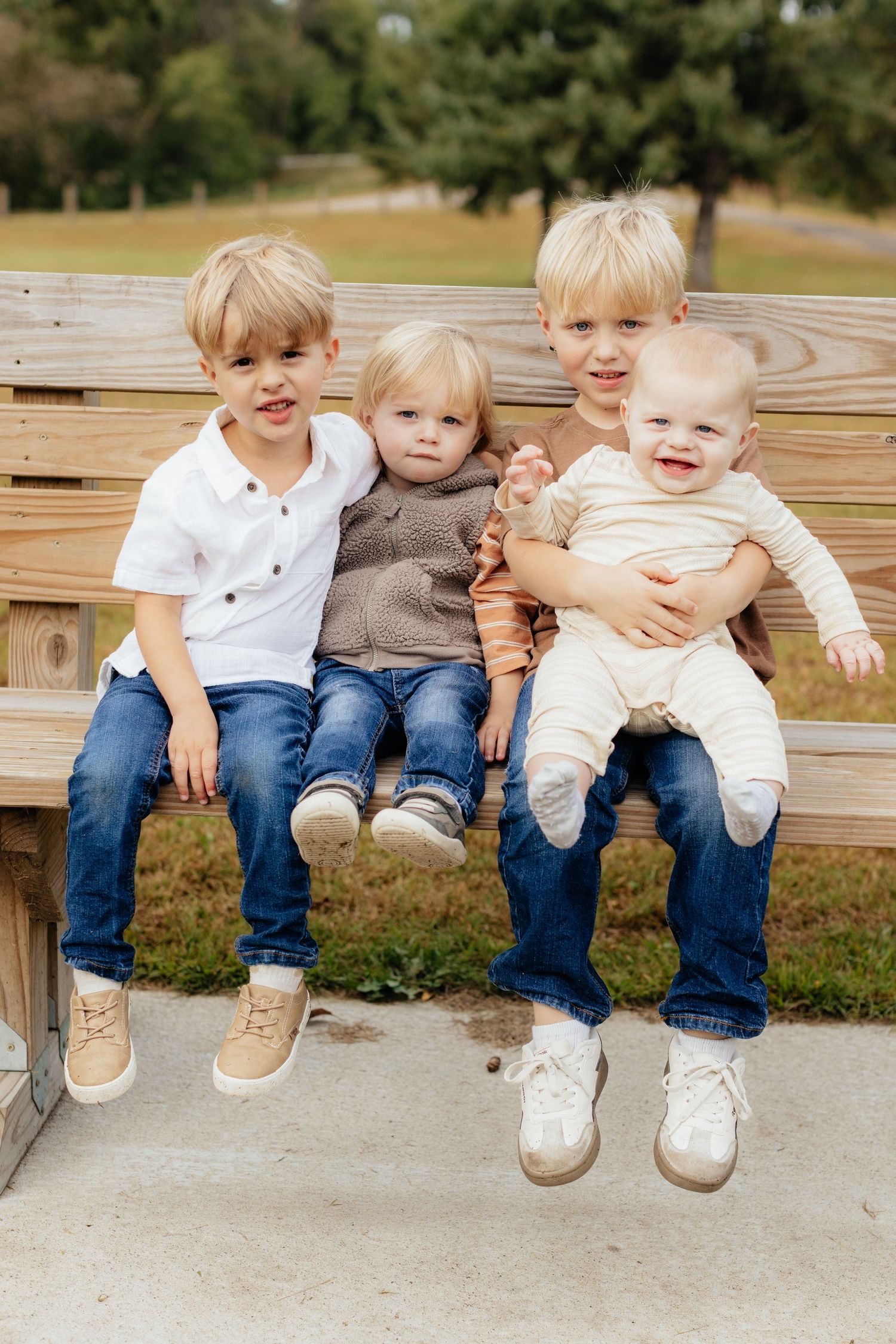 Young children sit together on a wooden bench wearing coordinated casual outfits.