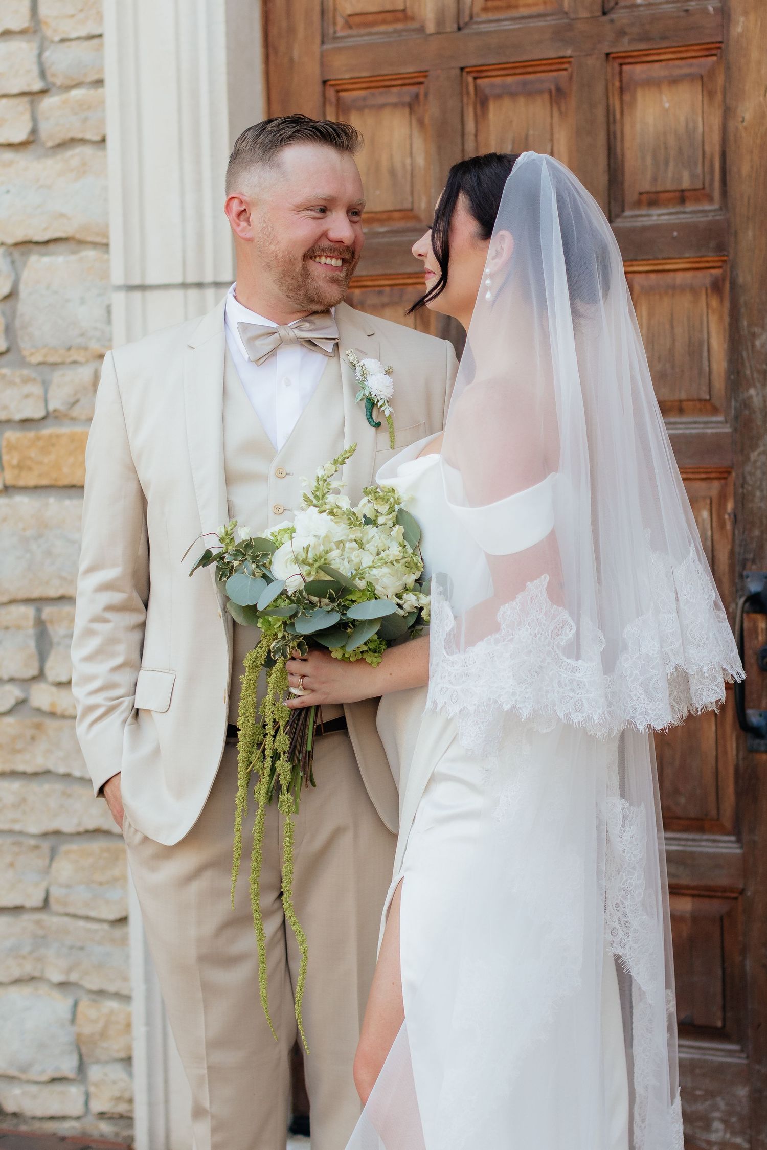 Wedding couple poses for romantic portraits against stone wall and wooden doors.