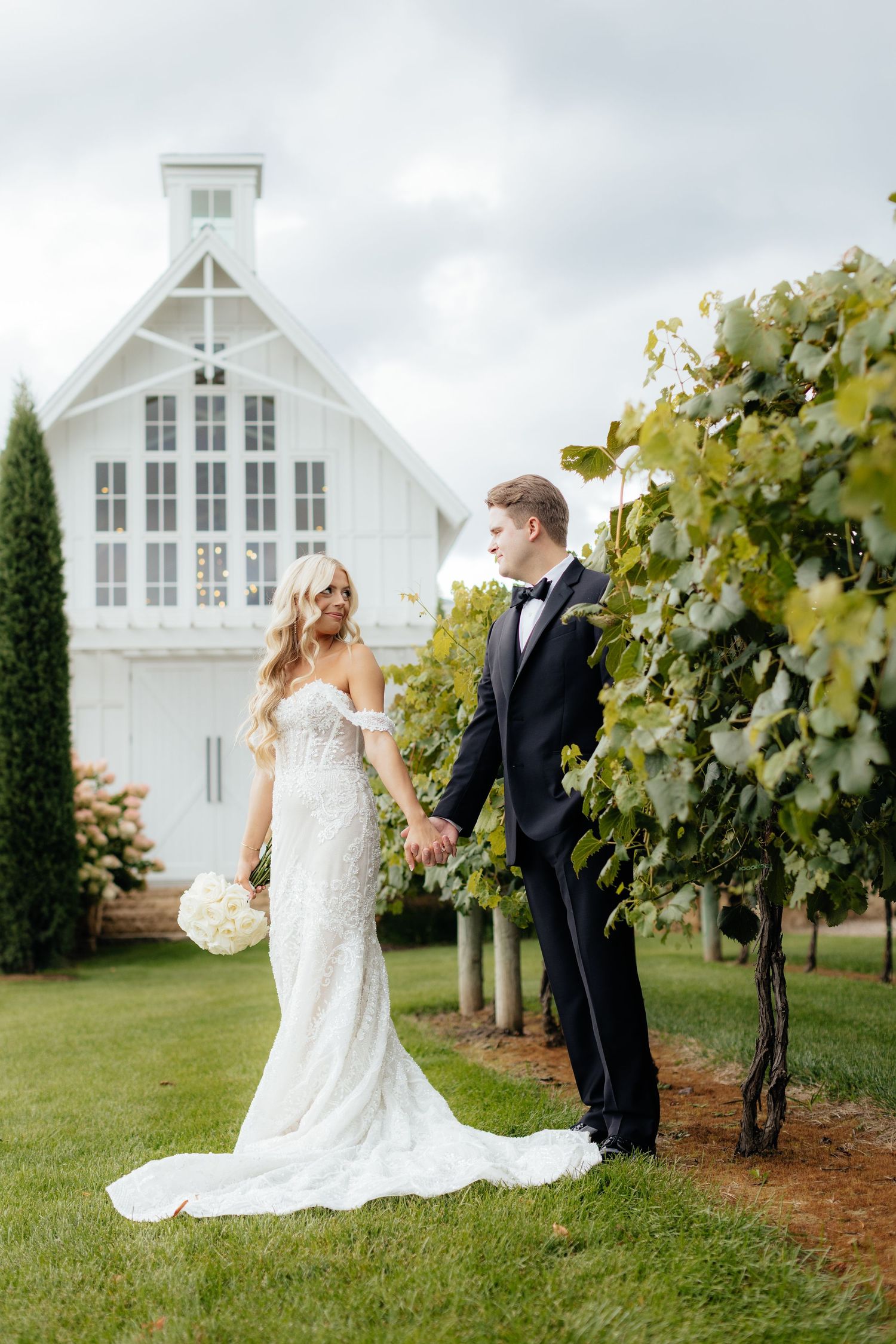 Romantic wedding portraits captured among vineyard rows with white chapel backdrop.