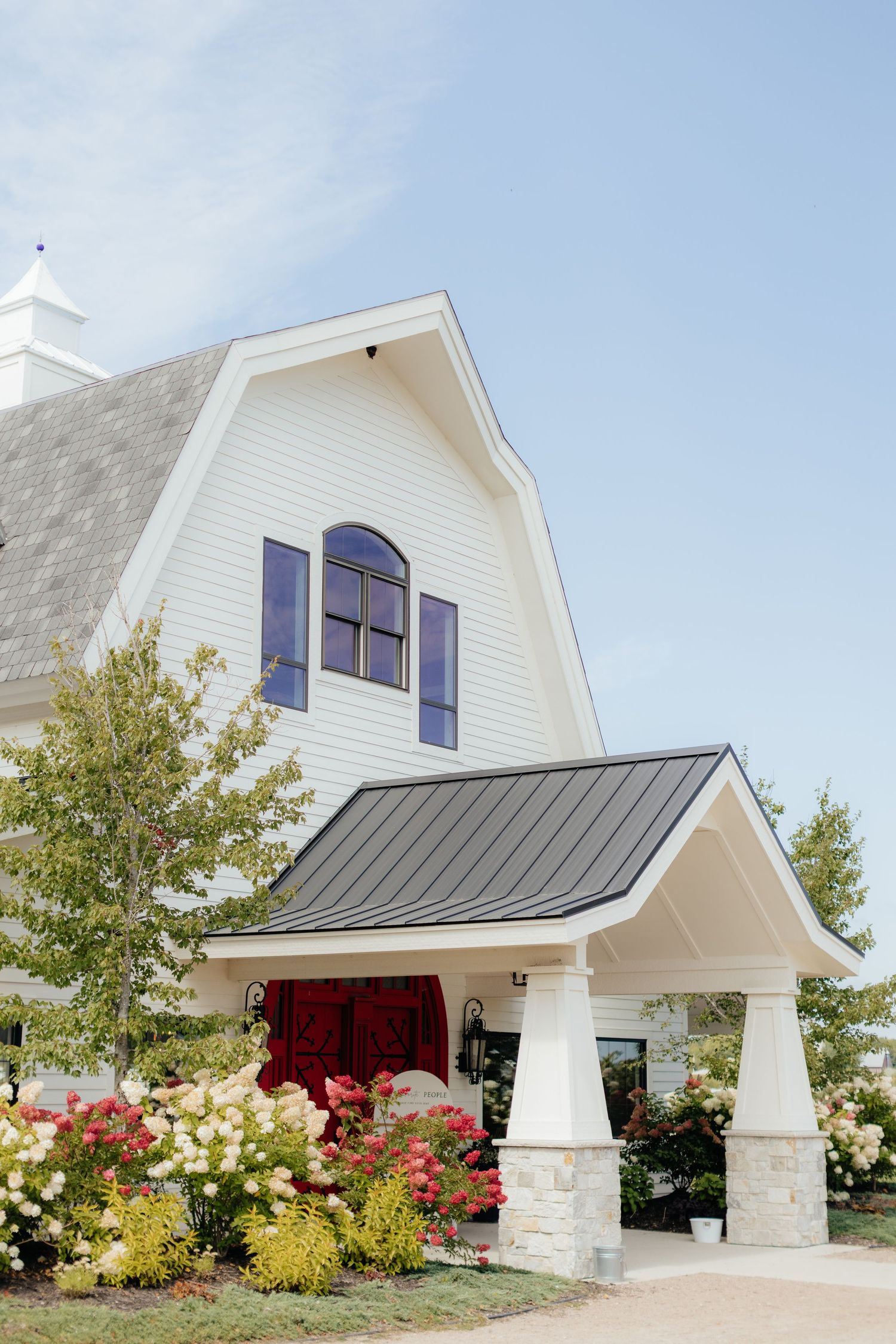 Modern white chapel with stone columns and colorful garden landscaping.