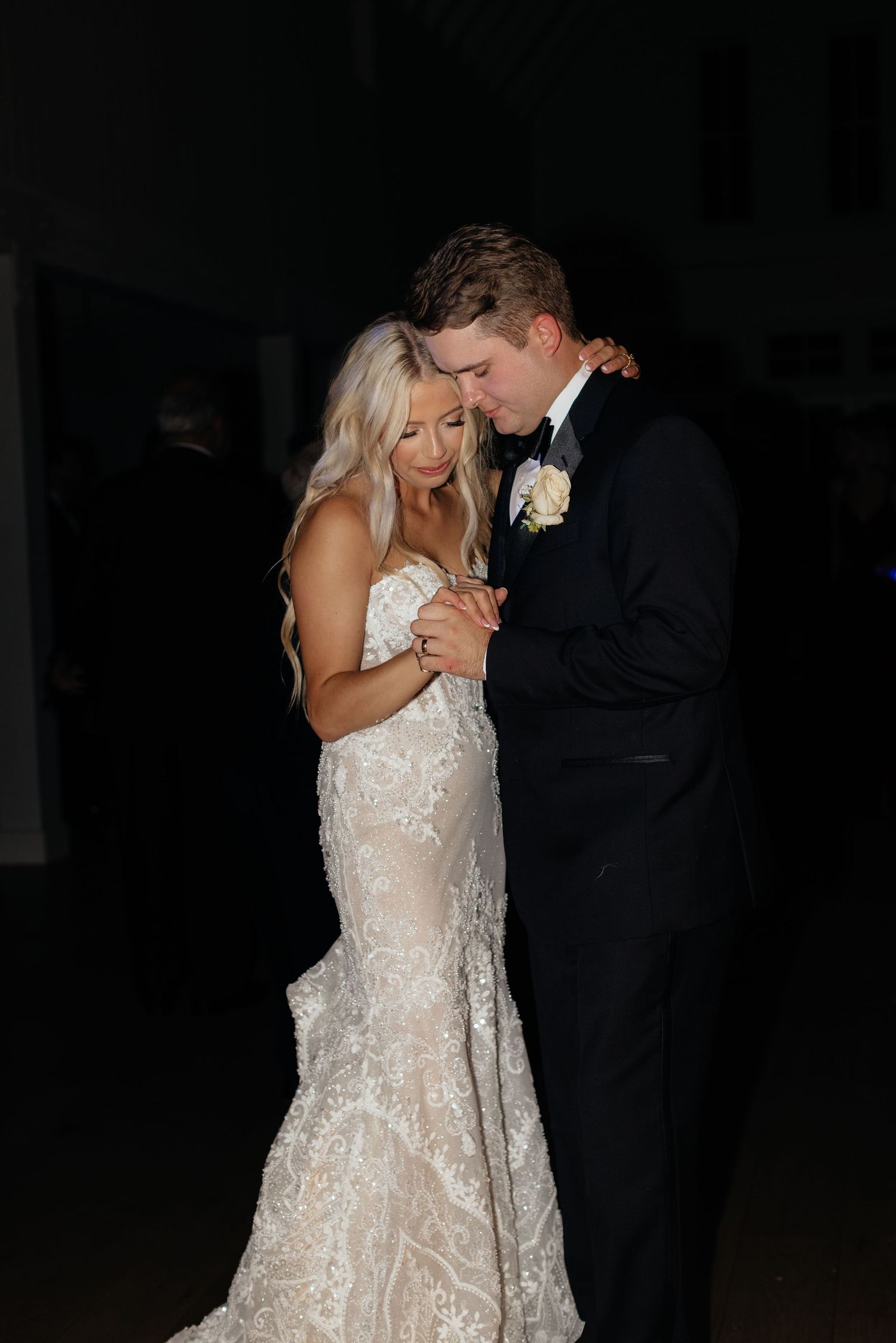 Intimate slow dance moment at wedding reception with bride in detailed white gown.