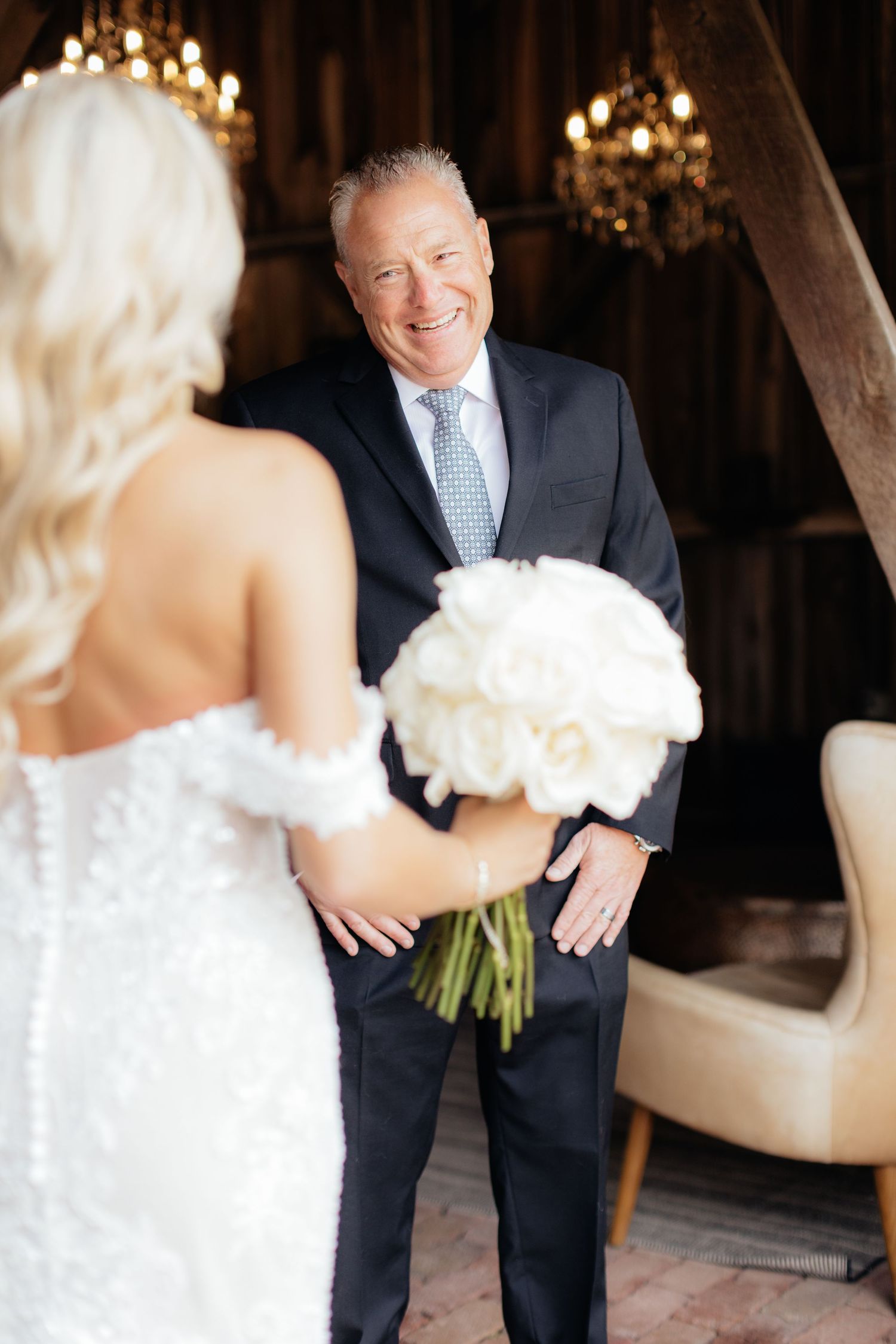 Candid wedding moments captured in rustic barn interior with chandelier lighting.
