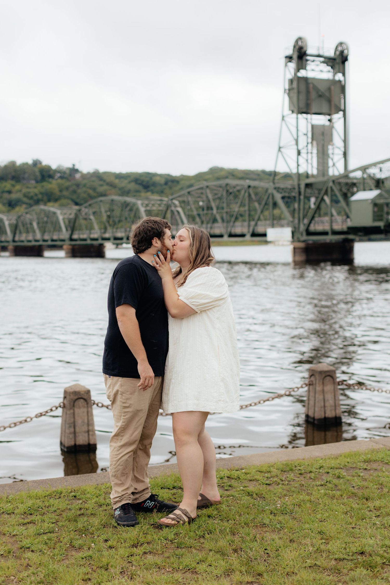 A romantic moment by the river with a historic bridge in the background.