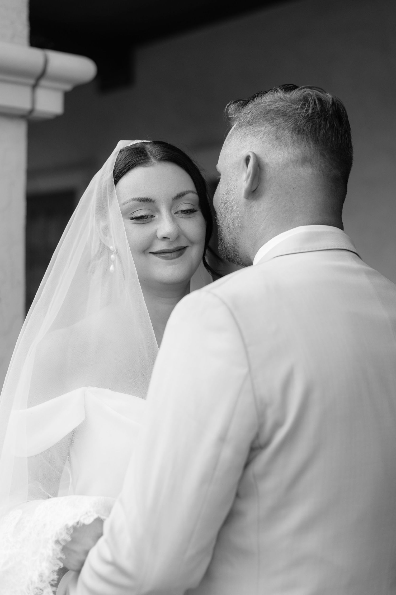 Intimate black and white wedding portrait showing tender moment between newlyweds under elegant white veil.
