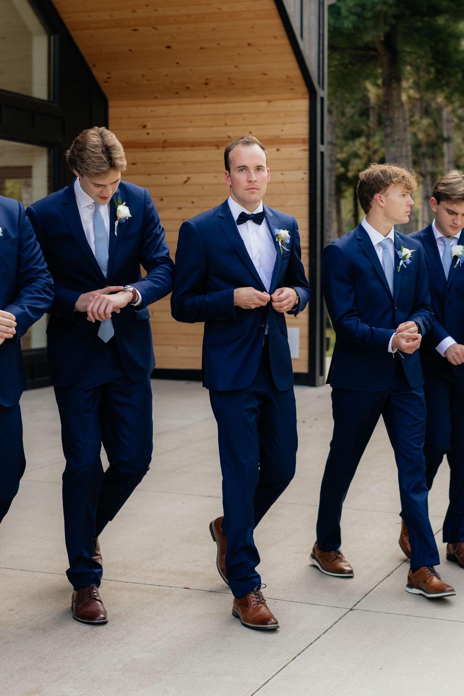 Groomsmen in navy suits show off their brown dress shoes in a playful series of poses.
