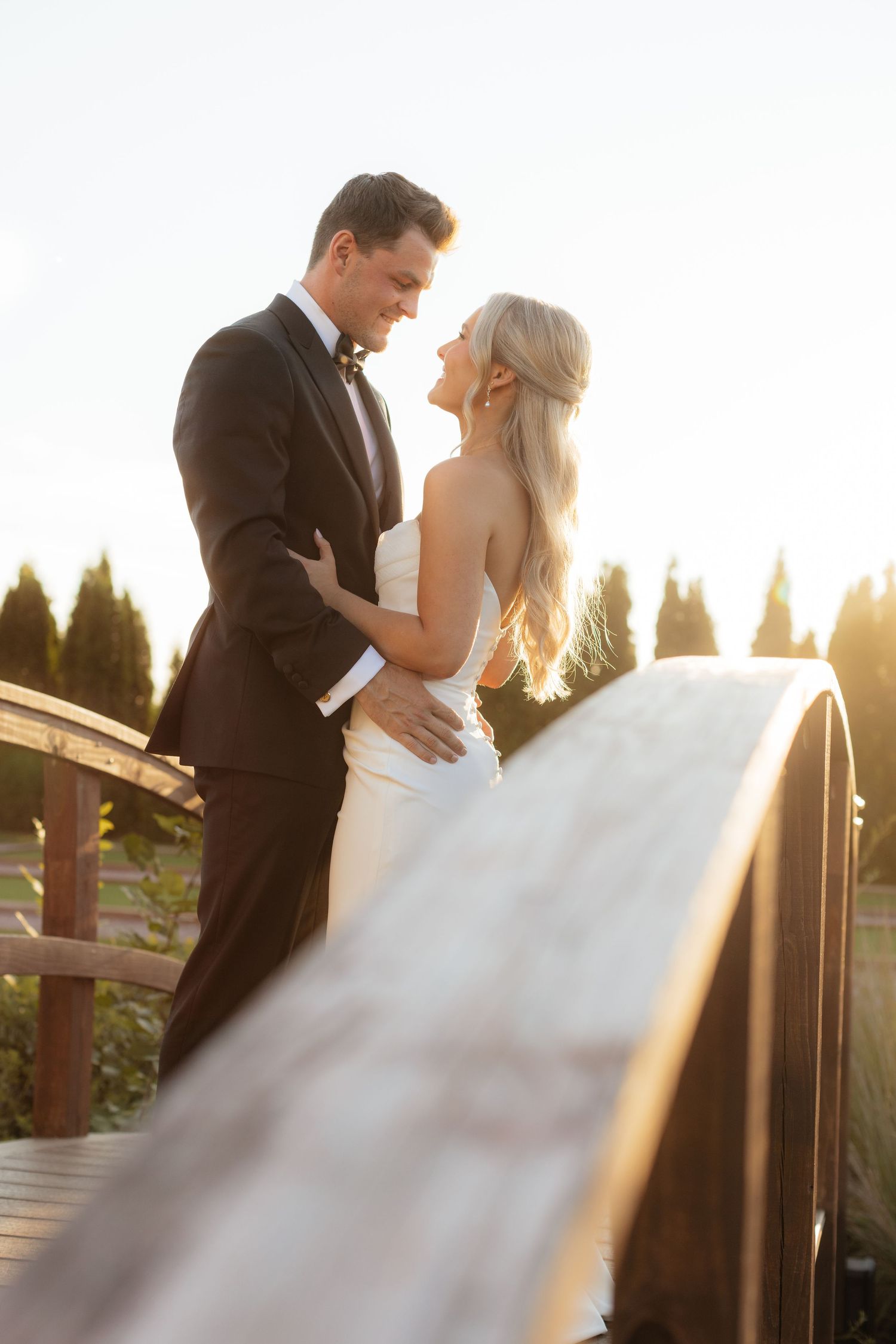 Wedding couple shares romantic moments on wooden stairs during sunset with golden light.