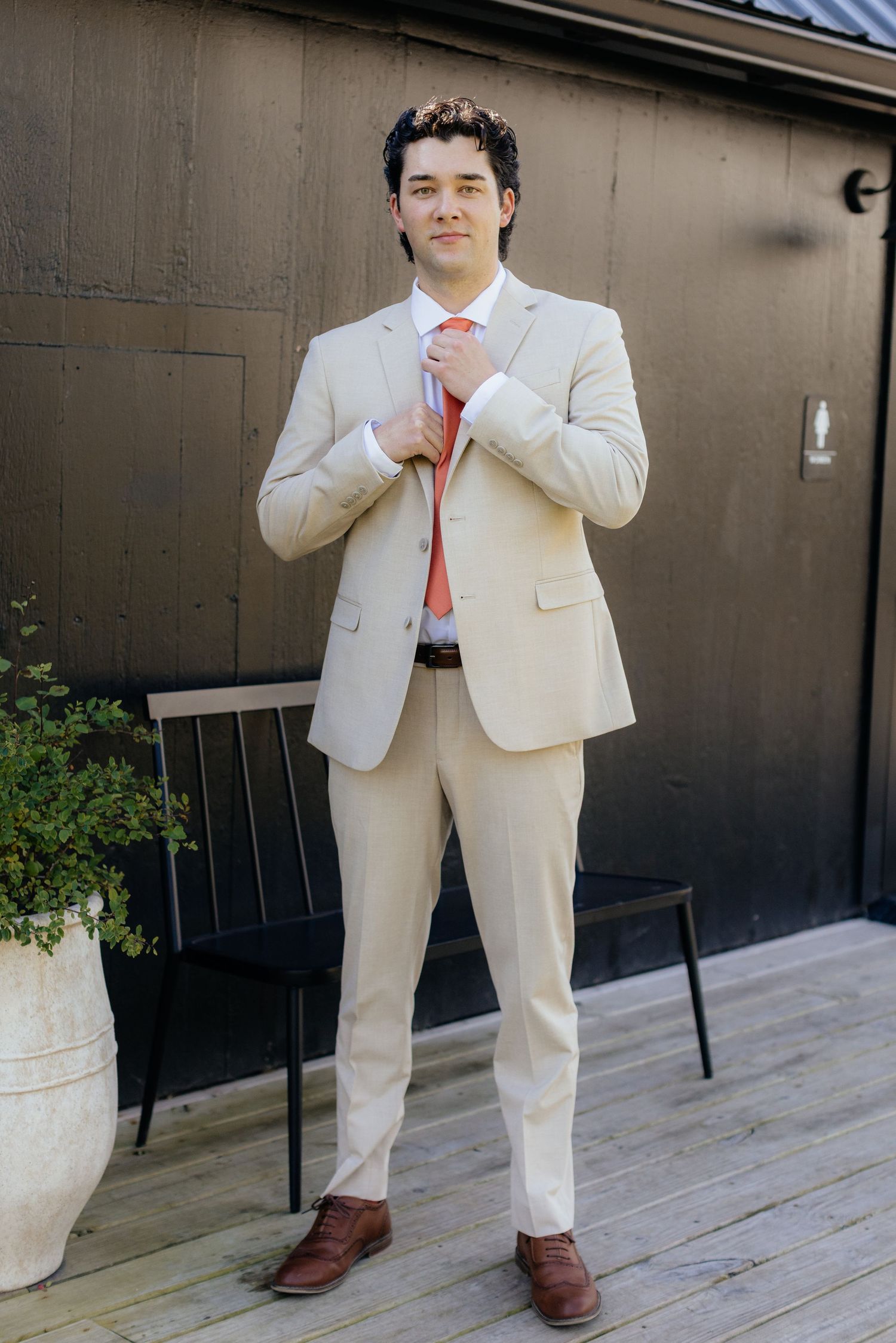 Someone in a cream colored suit poses playfully on an outdoor wooden deck.