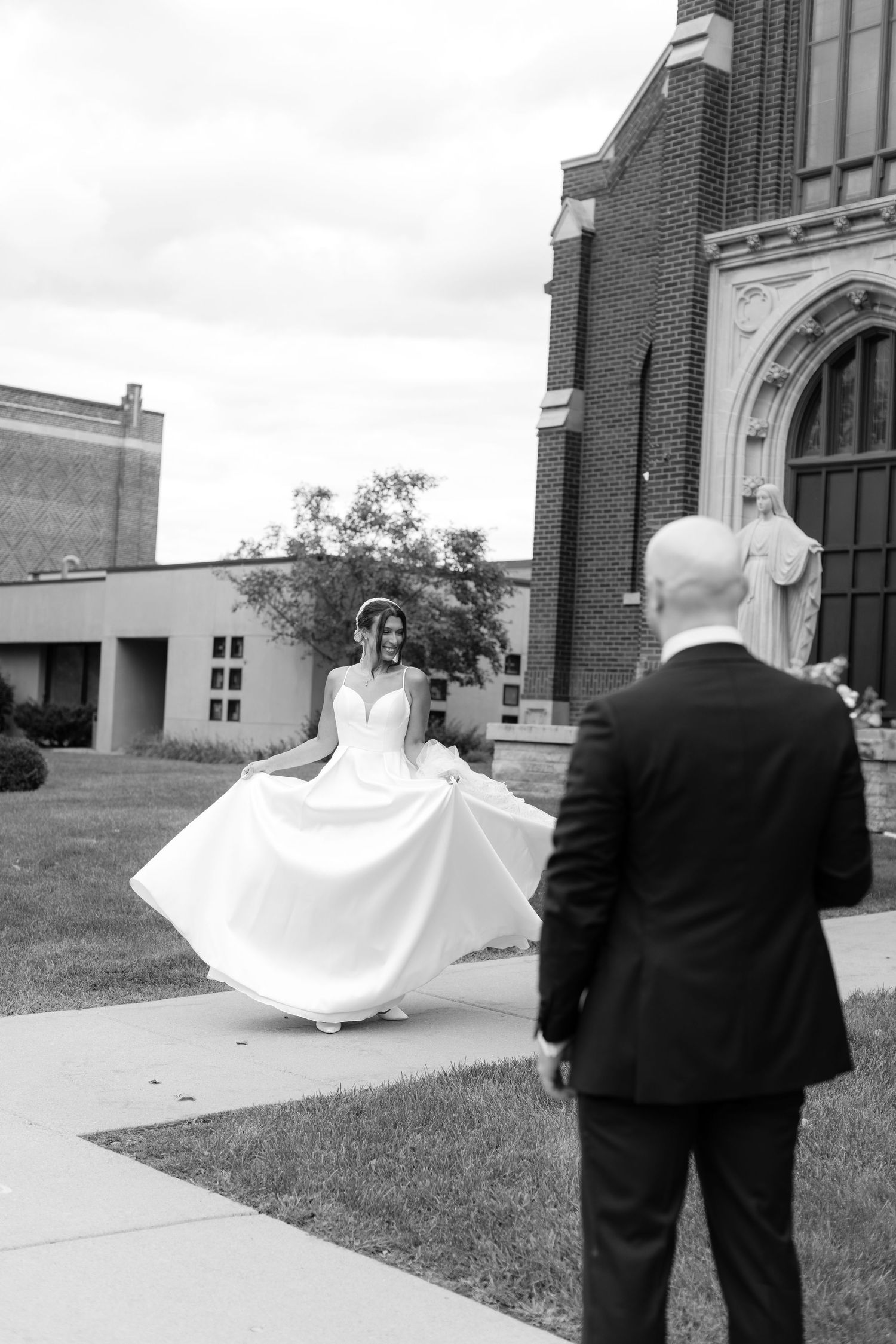 Couple in wedding attire walking outside a traditional brick church.