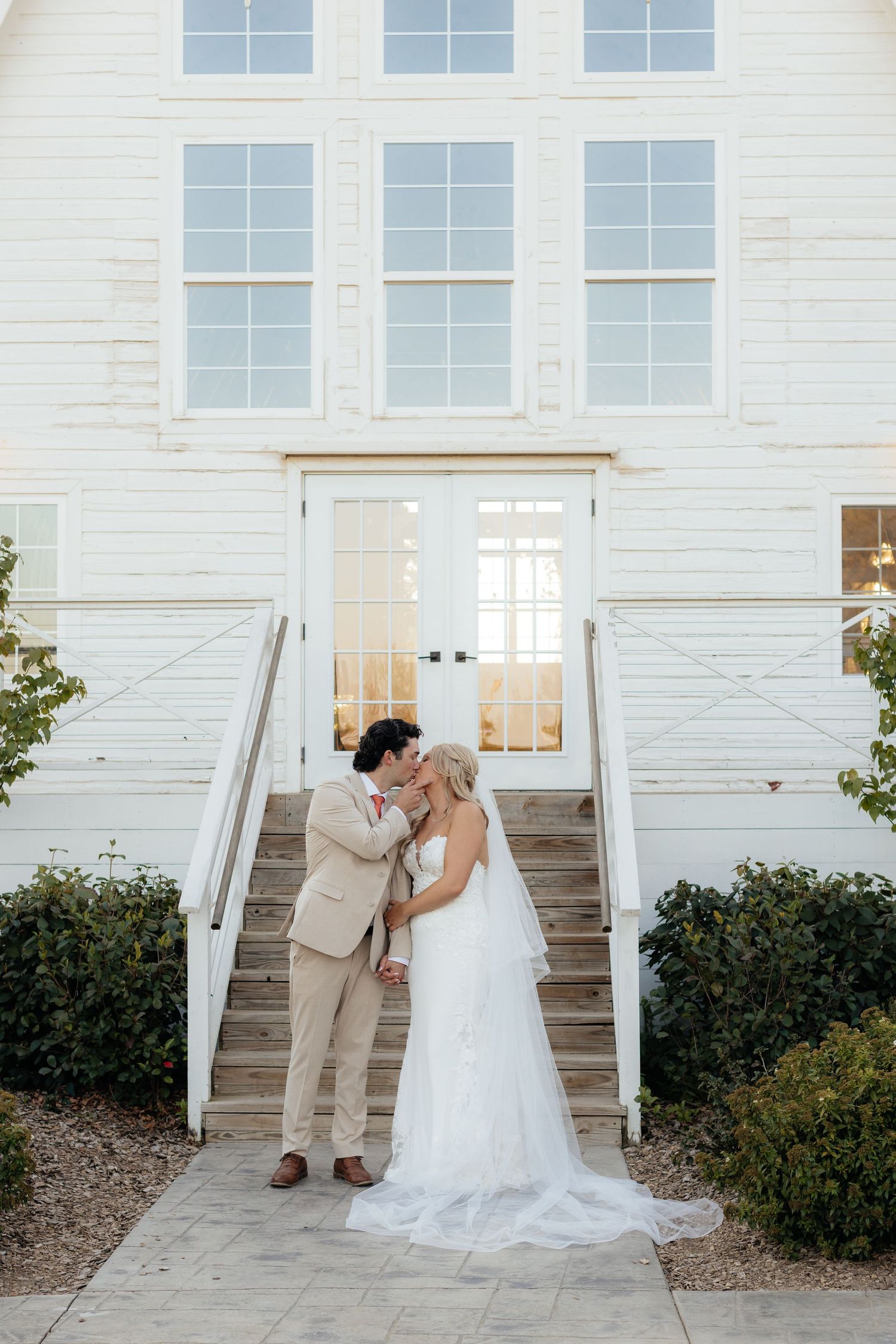 Wedding couple in white dress and tan suit posing on white stairs outside a chapel.