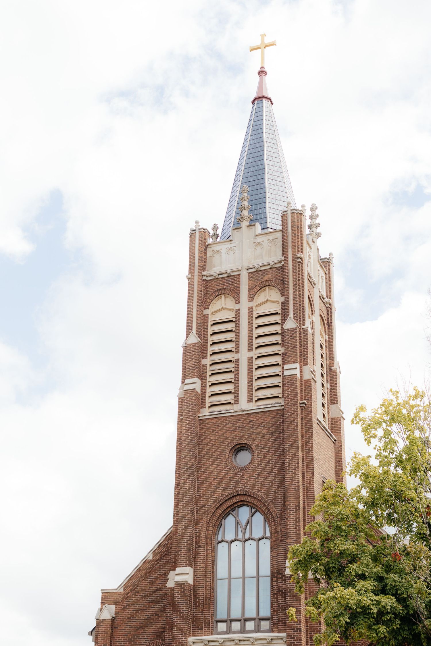 Gothic brick church exterior with tall spires and stained glass windows against cloudy sky.