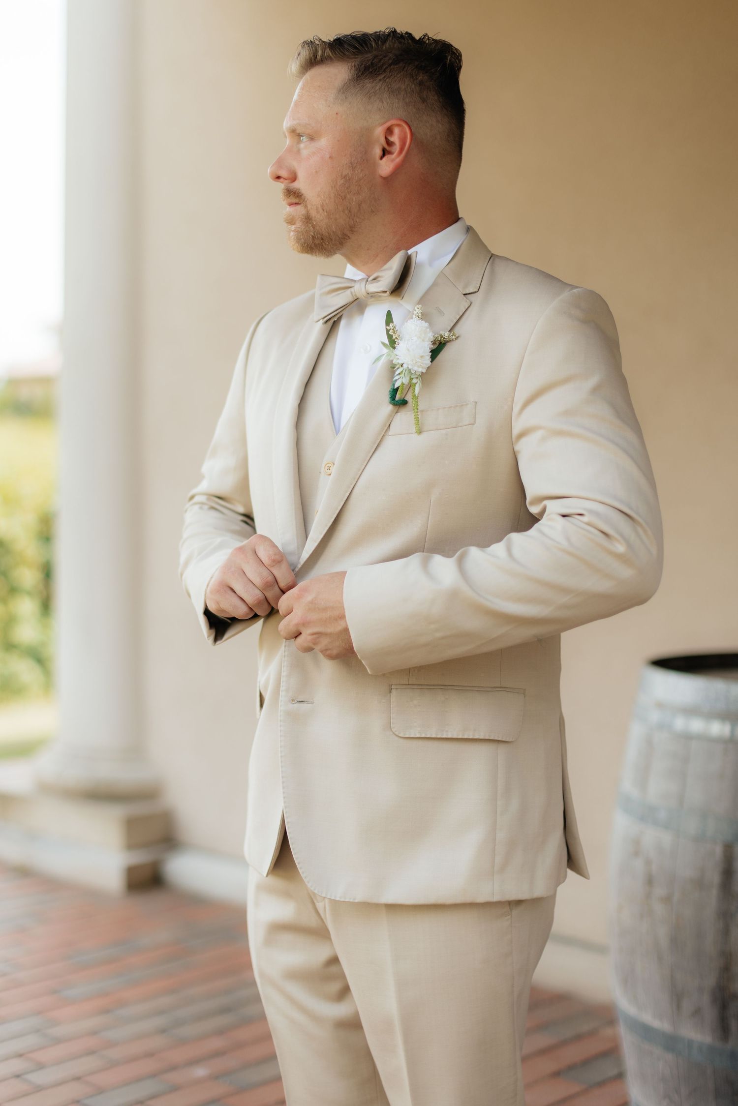 Groom in light beige suit adjusting his tie before the ceremony.
