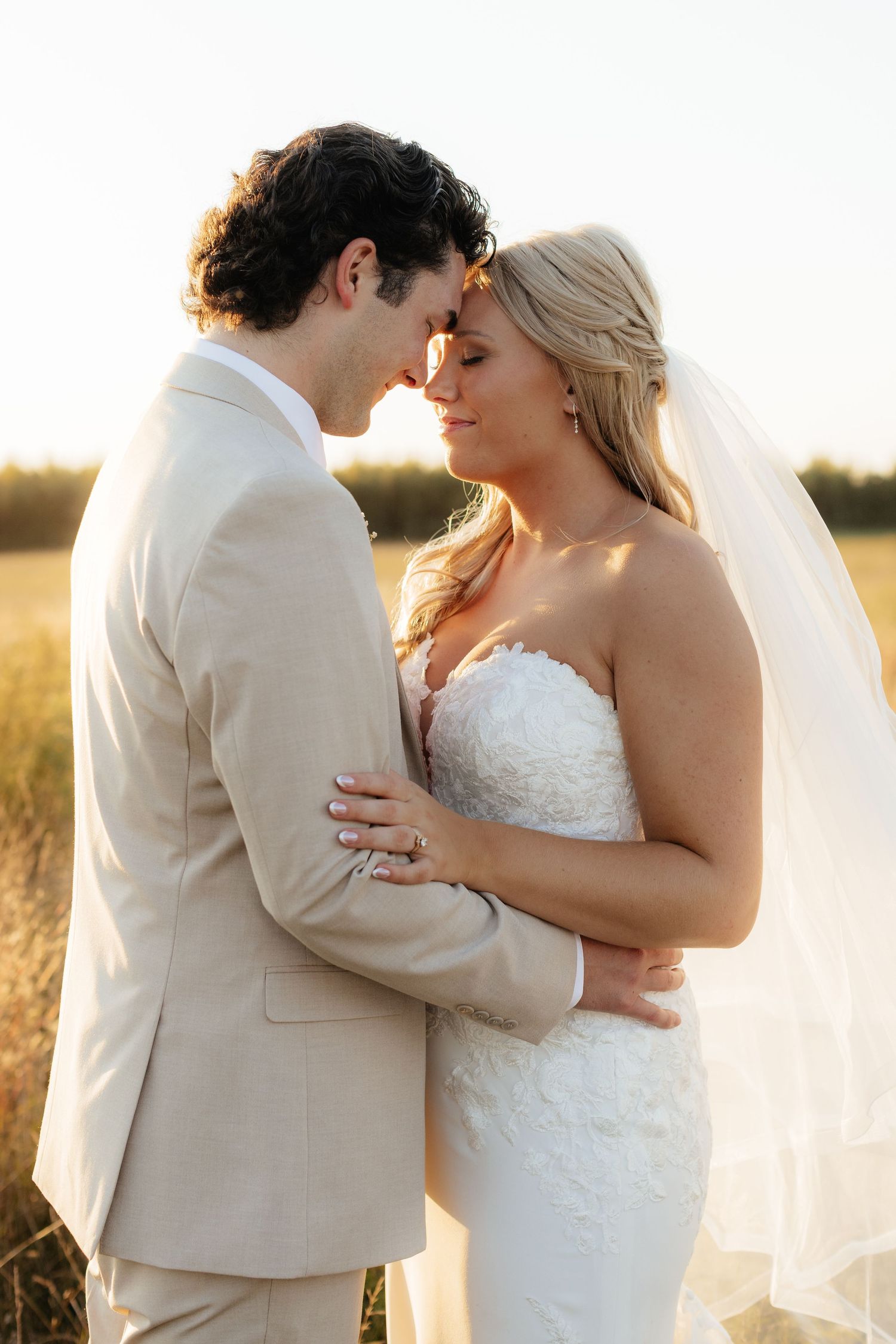 Romantic wedding couple embracing in a golden field at sunset.