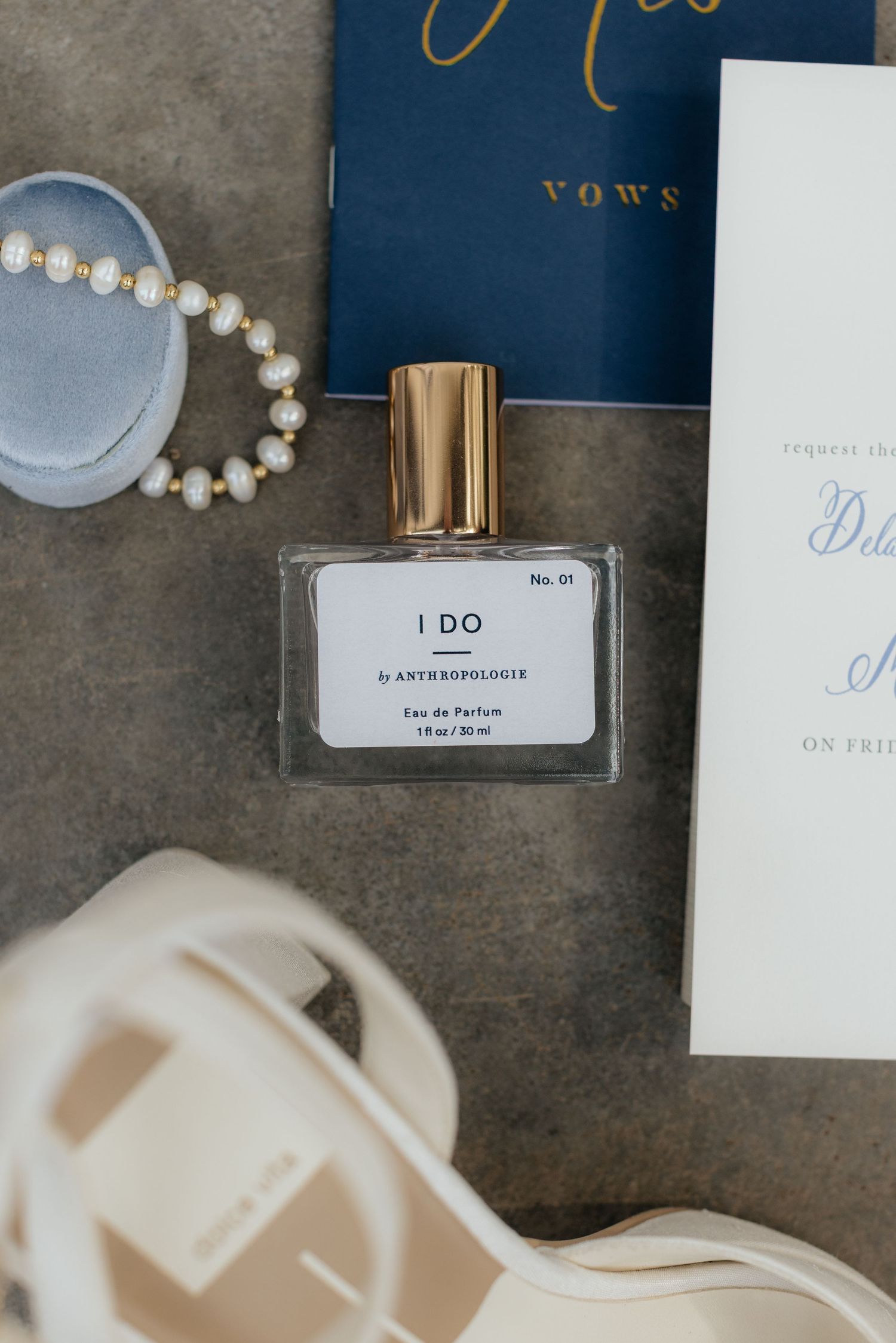 Wedding details including perfume bottle labeled 'I DO', vow book, and pearl accessories.