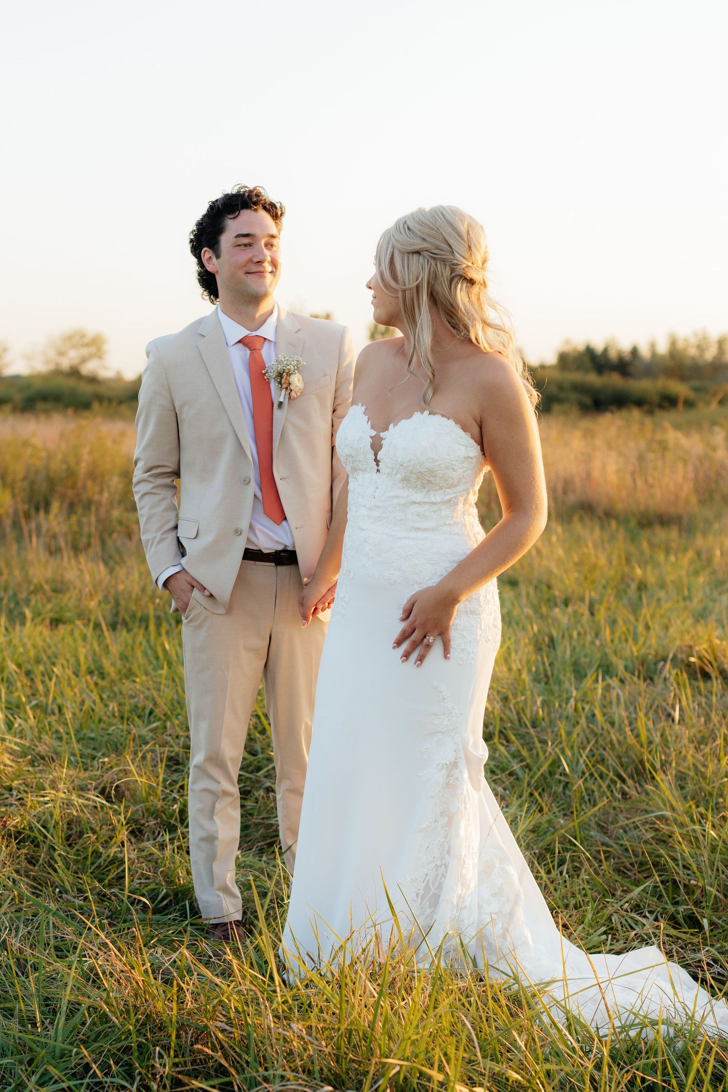 Candid wedding photos of couple walking through sunset field.
