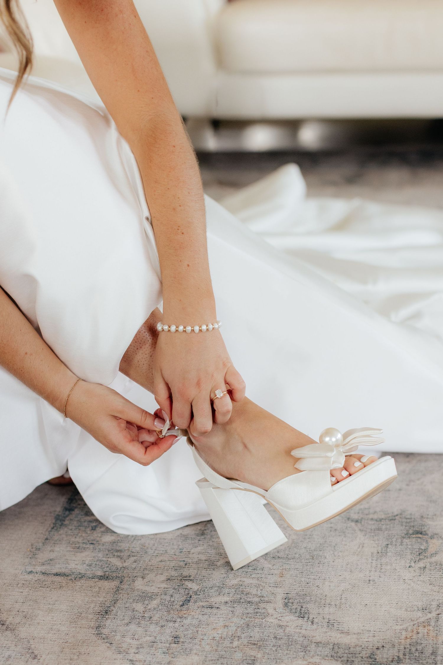 Close-up of bride putting on elegant white wedding shoes.