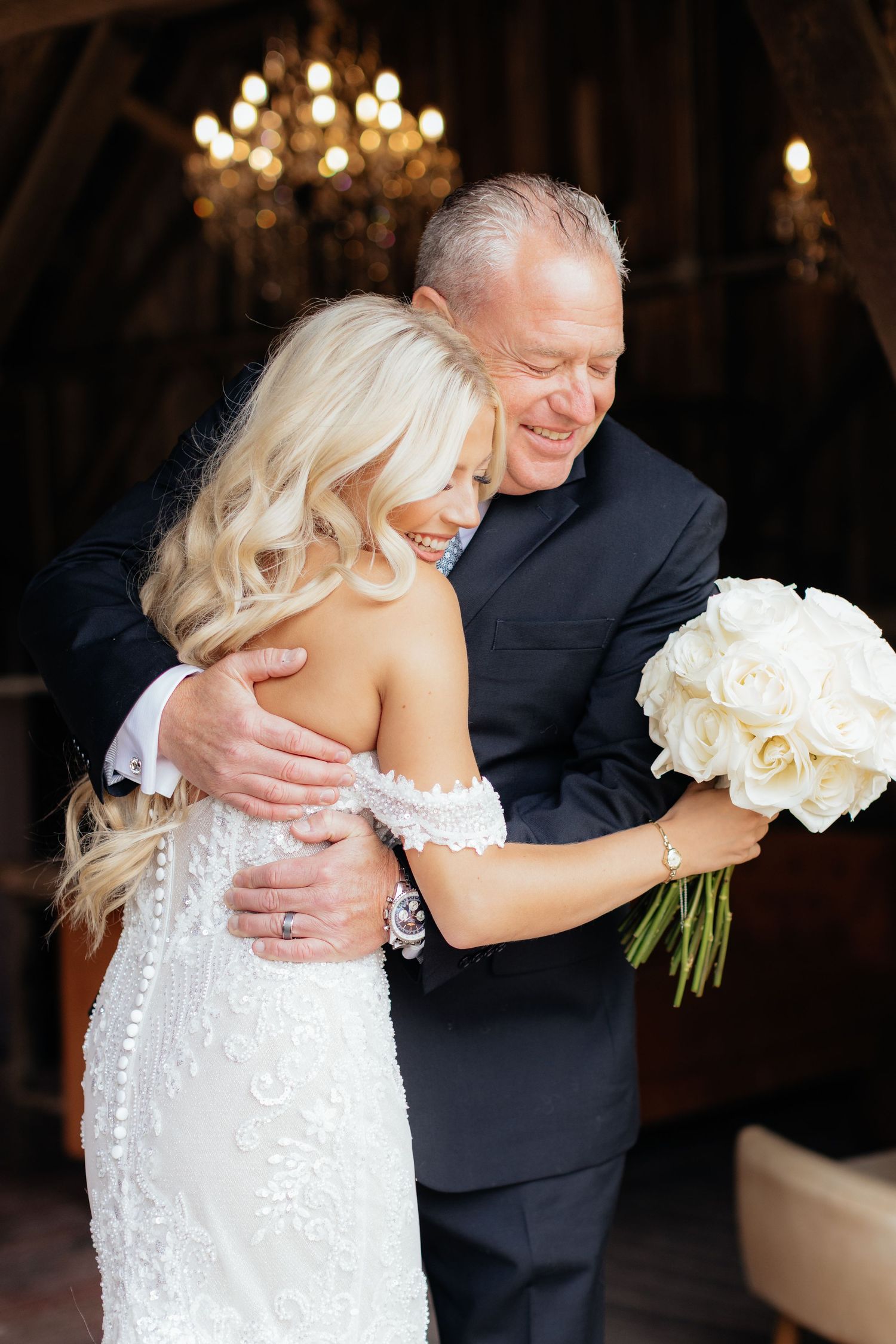 Wedding couple embraces in a dimly lit venue with elegant chandeliers overhead.