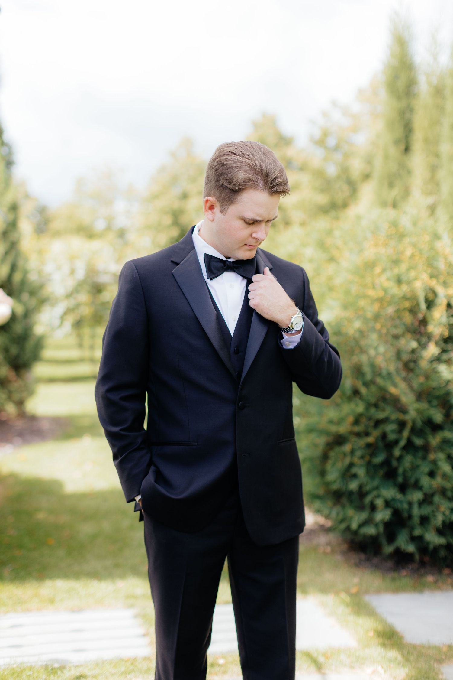 Formal black tuxedo and bowtie against an outdoor garden setting.