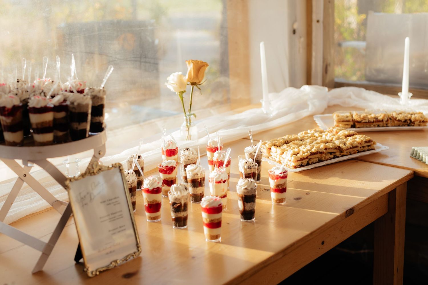 Dessert table with parfaits and treats displayed near a window with string lights.