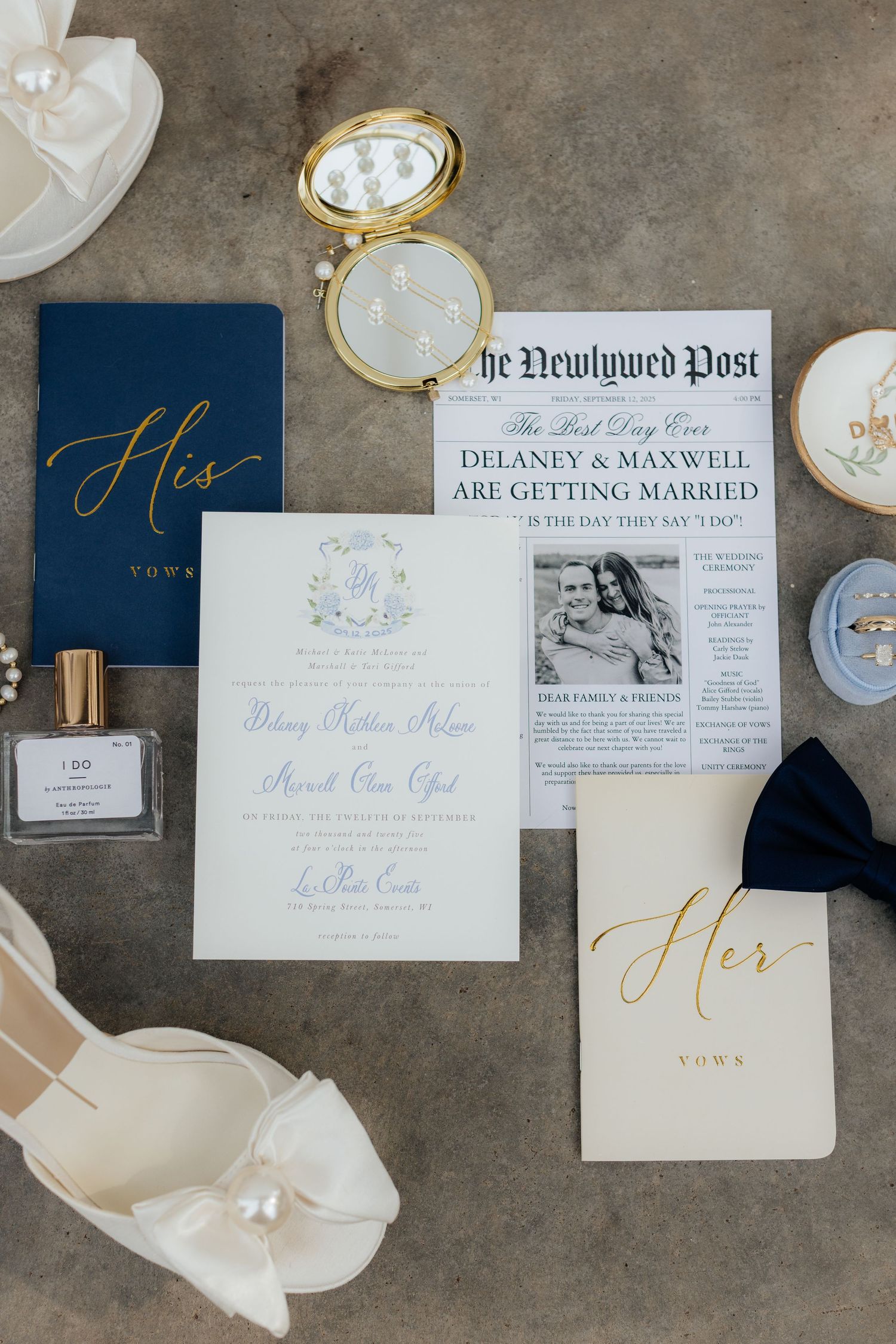 Wedding stationery flat lay featuring navy and gold vows books, invitation suite, and newspaper-style announcement.