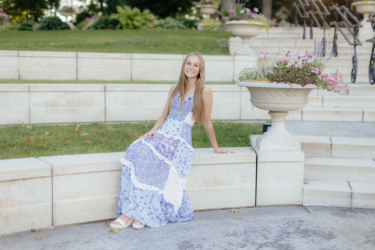 A blue and white floral maxi dress worn on stone steps in a garden setting.