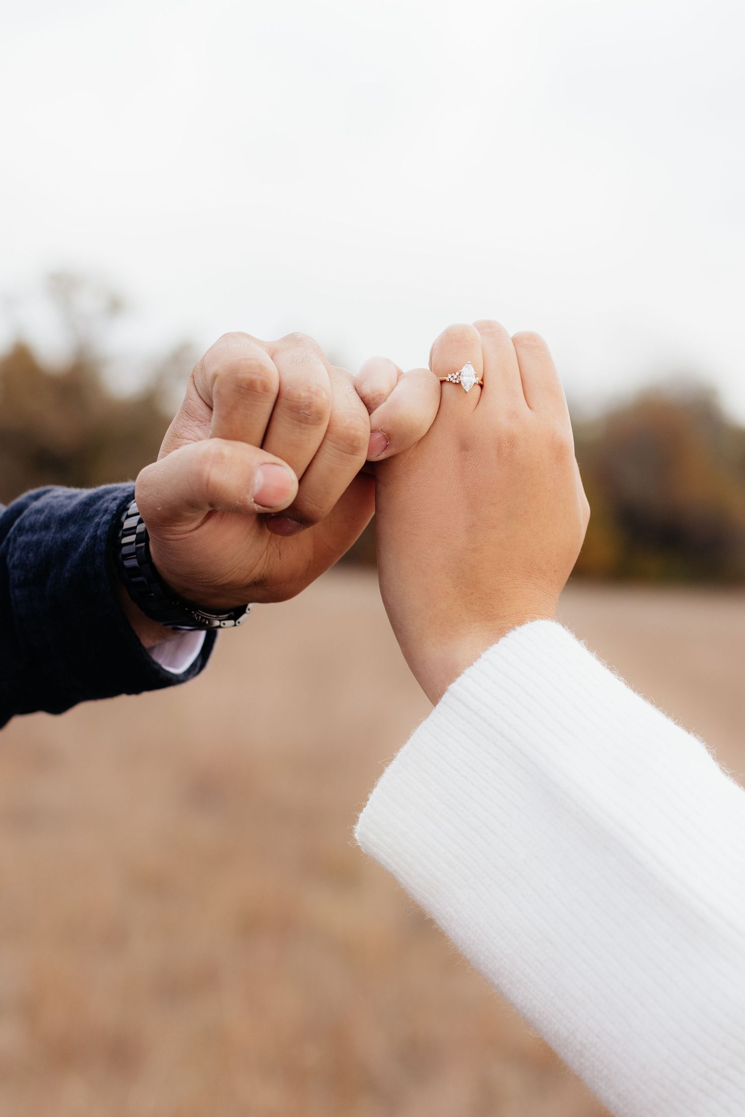 Close-up of pinky promise hands with engagement ring visible.