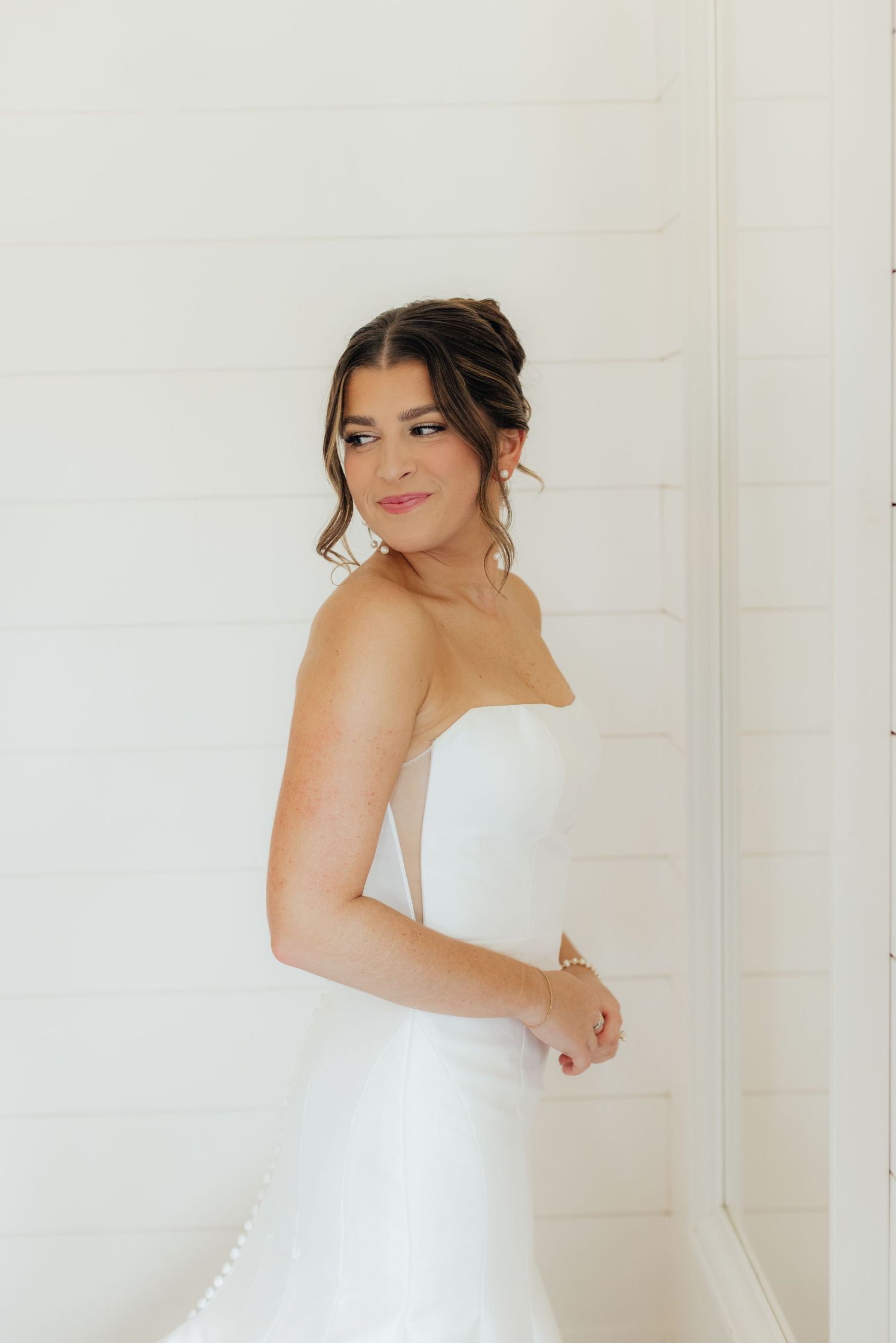 A bride in a strapless white wedding gown poses against a light background.