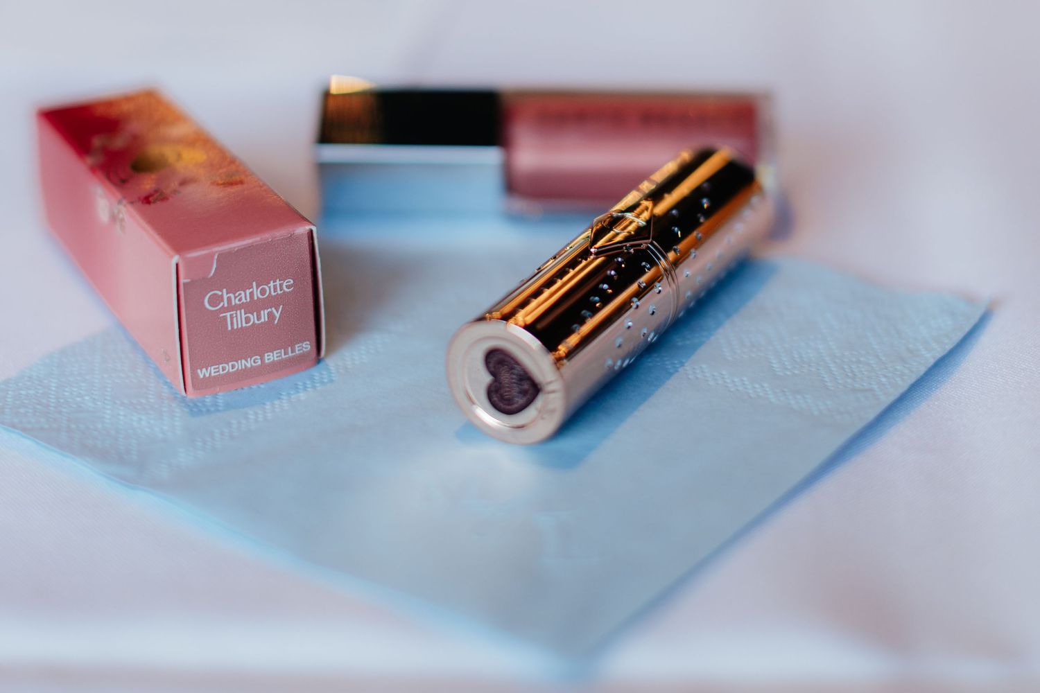 Soft focus beauty products in pink packaging on pale blue background.