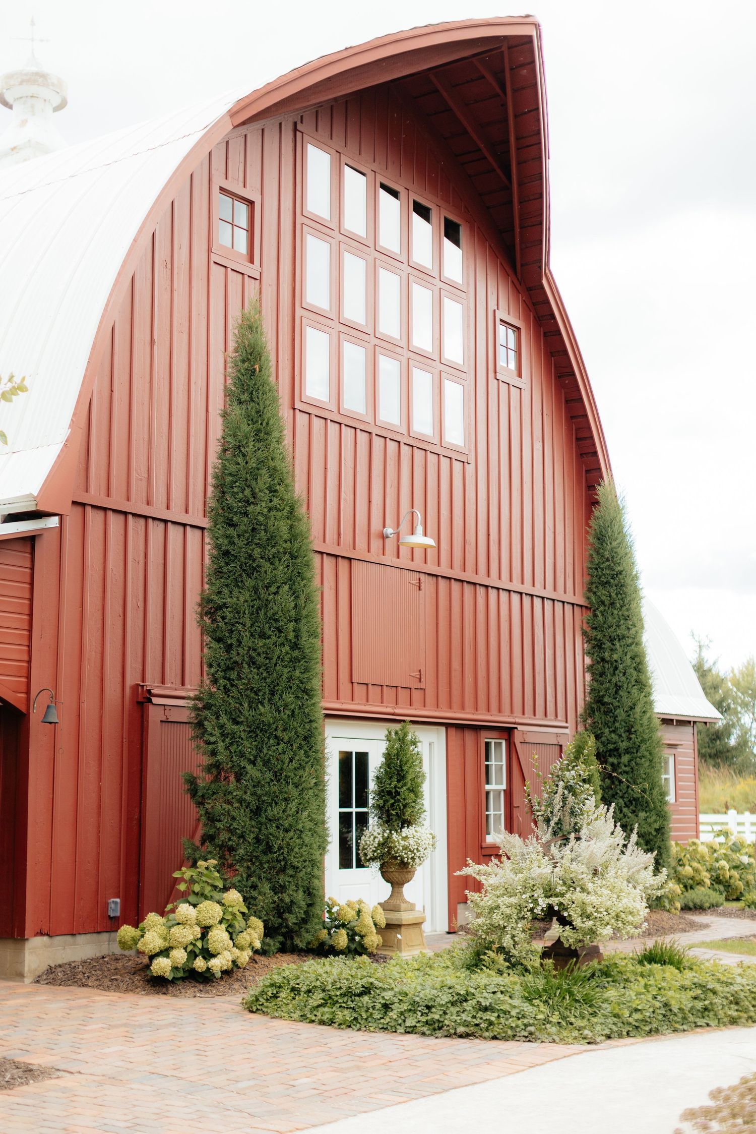 Red barn with white trim and evergreen trees along the exterior in a rustic farm setting.