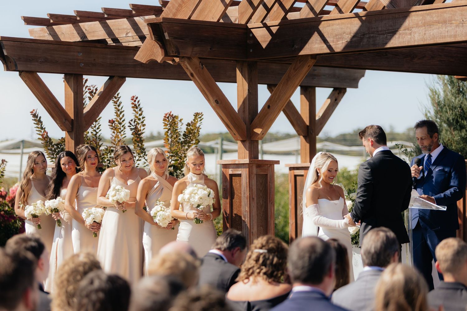 Wedding ceremony attendees gathered under a rustic wooden pavilion.