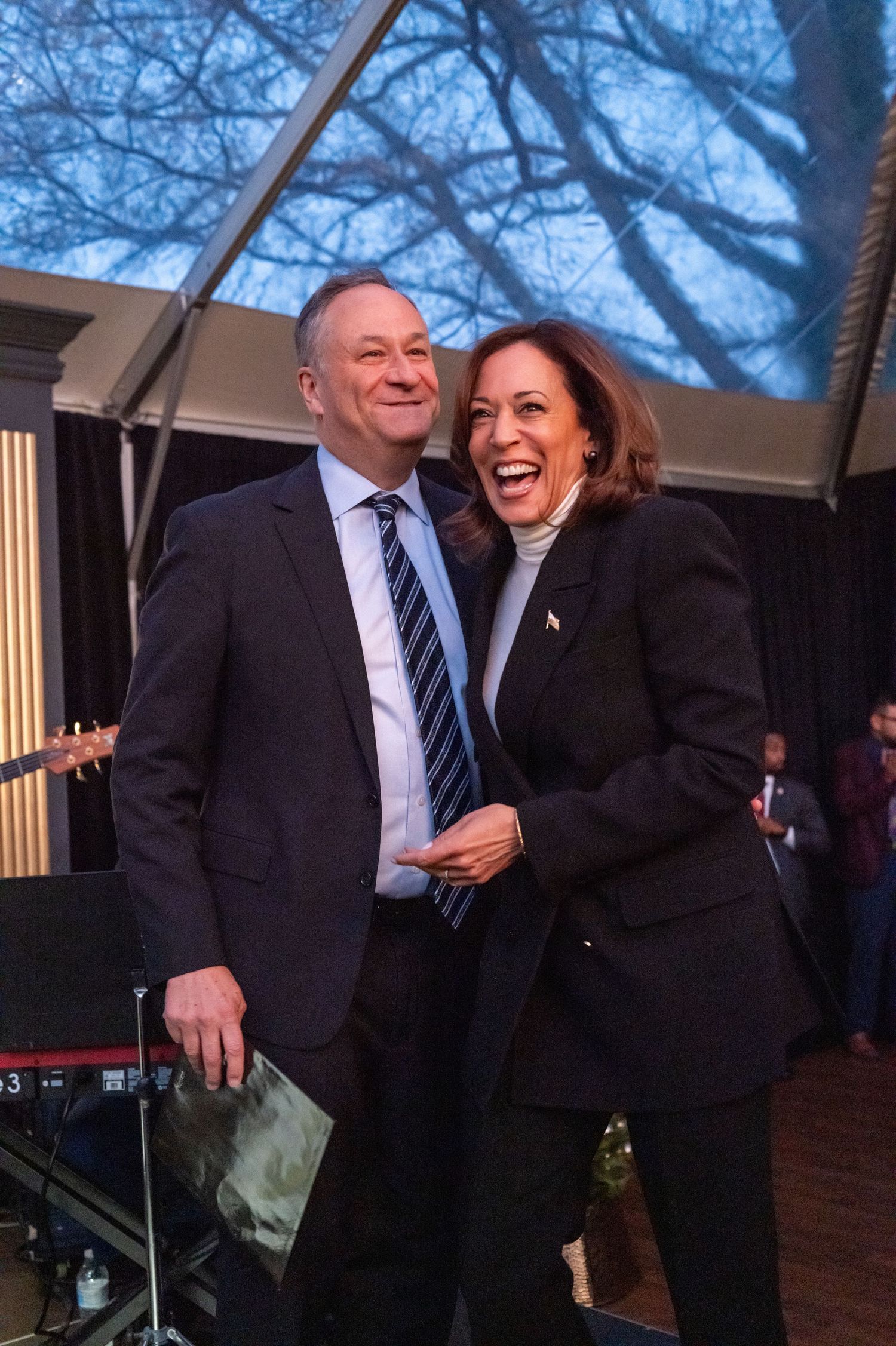 Two people share a laugh during a political event against a blue-tinted background.