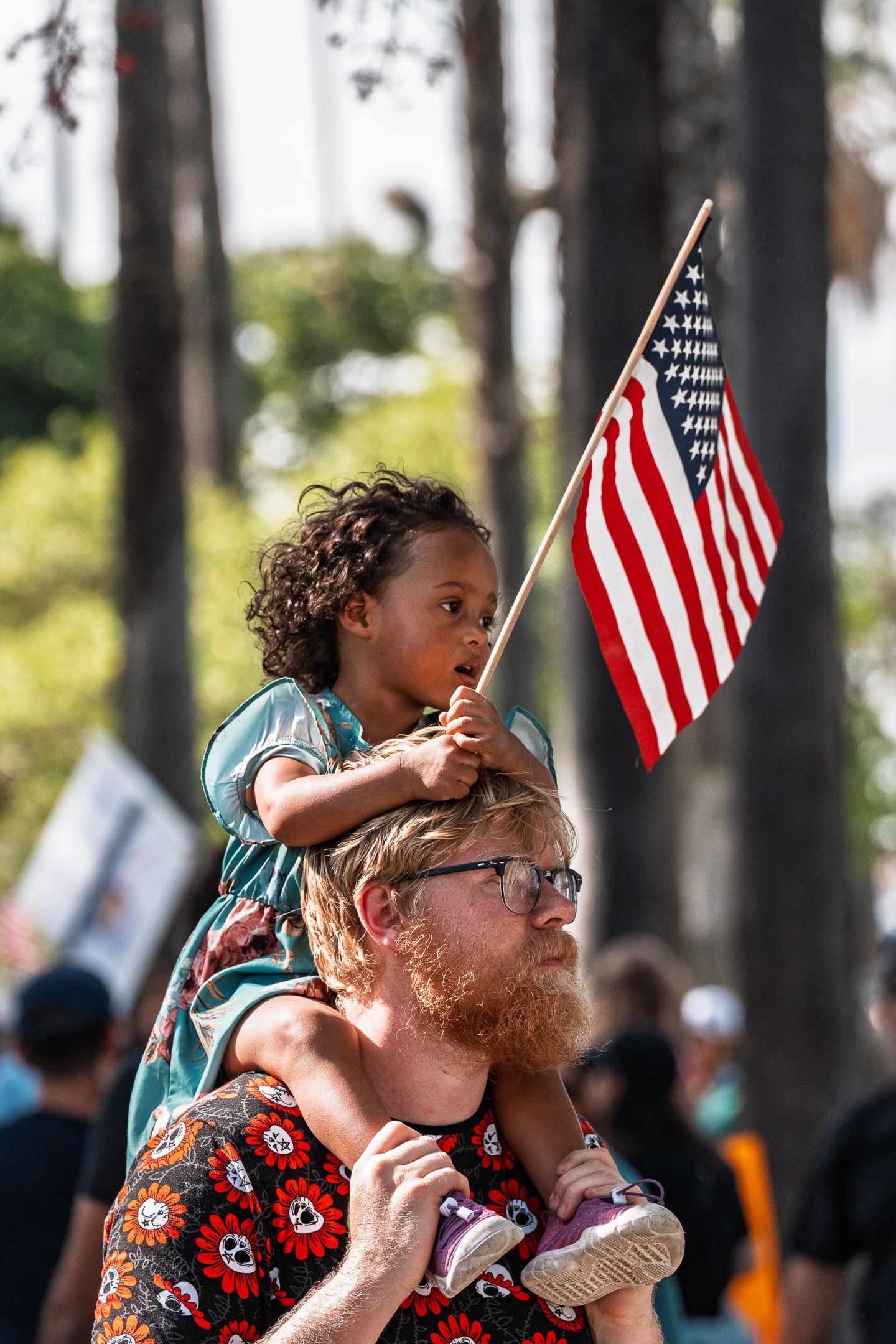 People gather at an outdoor event with American flags against a backdrop of trees.