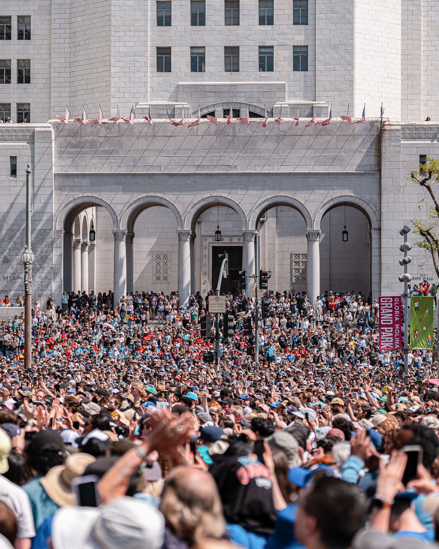 Large crowd fills courtyard outside white stone building during political gathering.