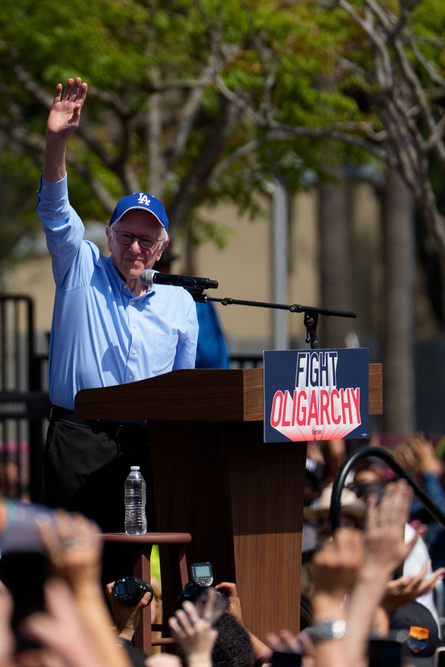 A speaker gestures enthusiastically while speaking at a podium during an outdoor rally.