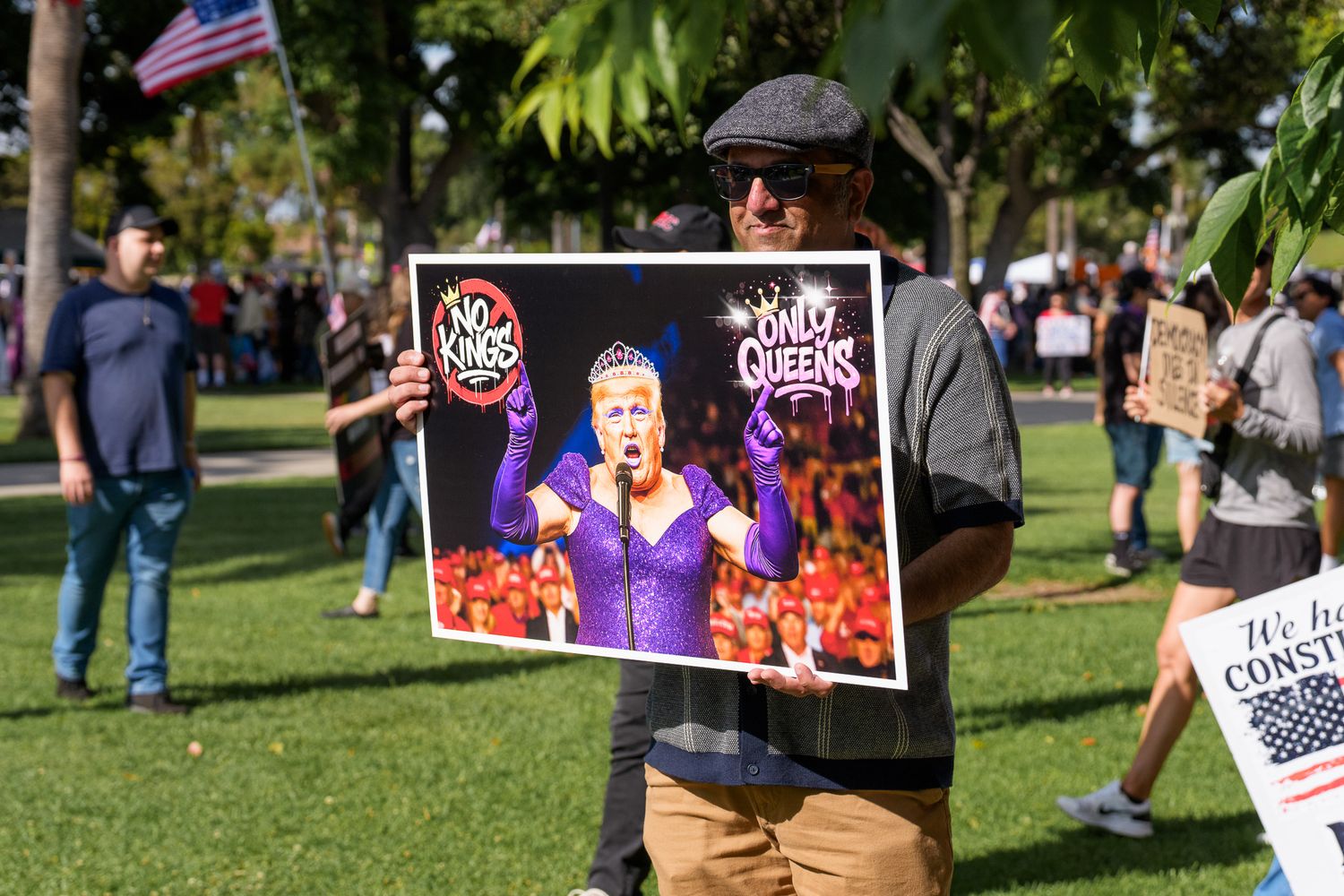 Crowd gathers in a park with protest signs and flags during a demonstration.