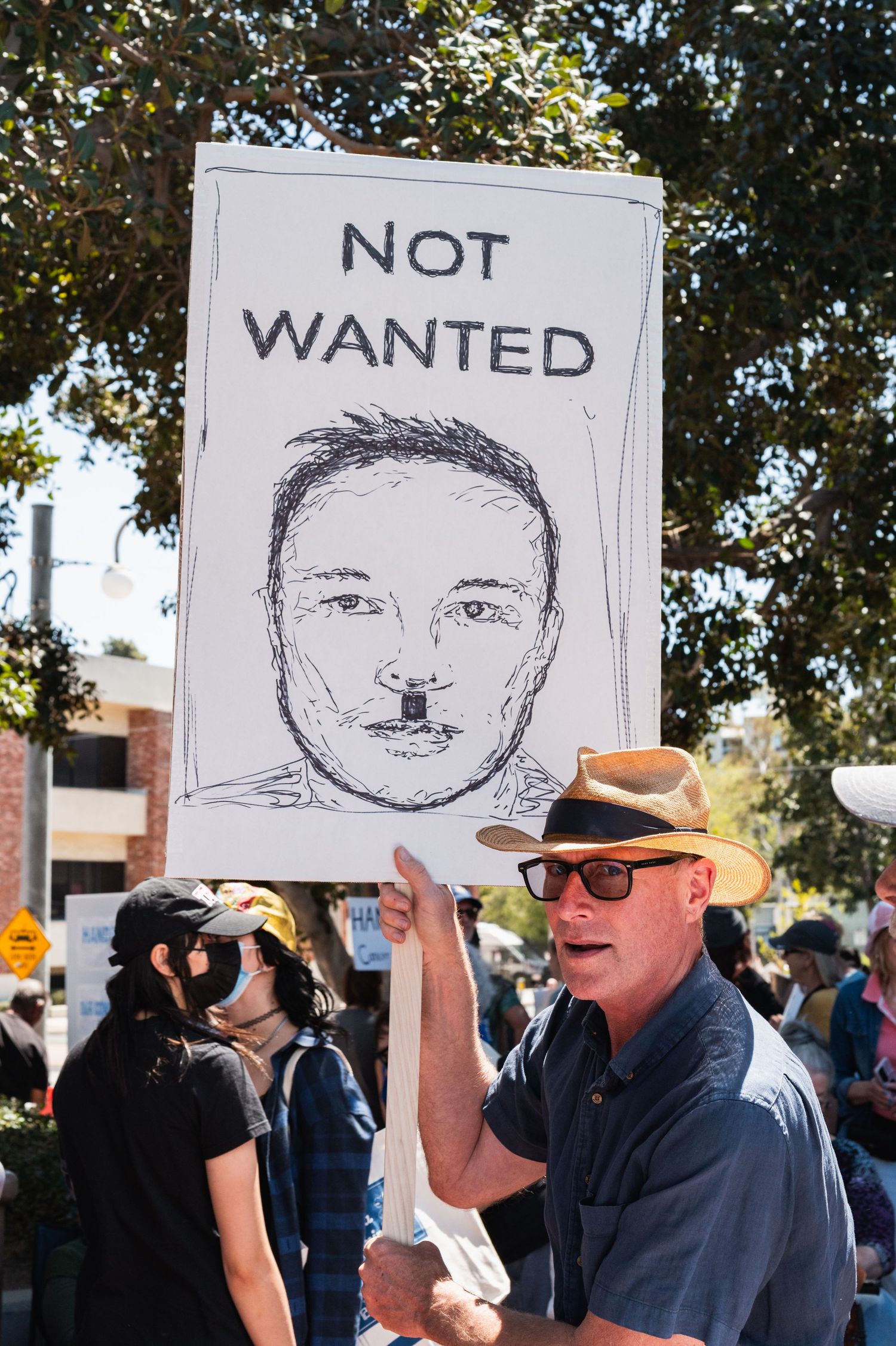 Demonstrators displaying protest signs with sketched portraits outdoors.