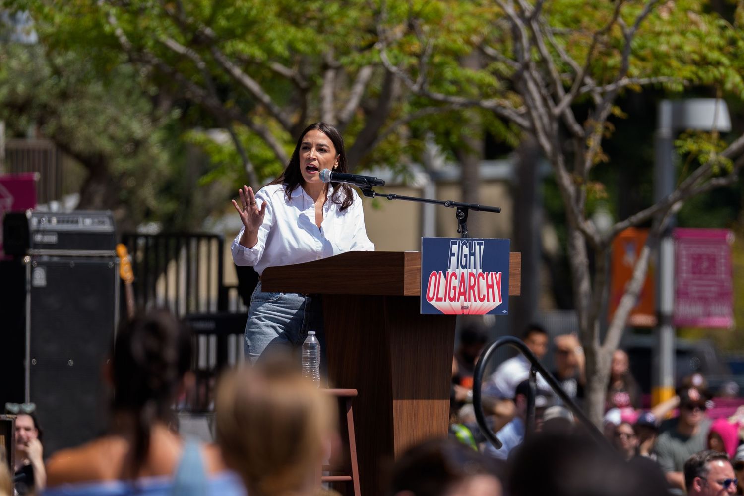 Political rally scene with podium and signs against a backdrop of trees and buildings.