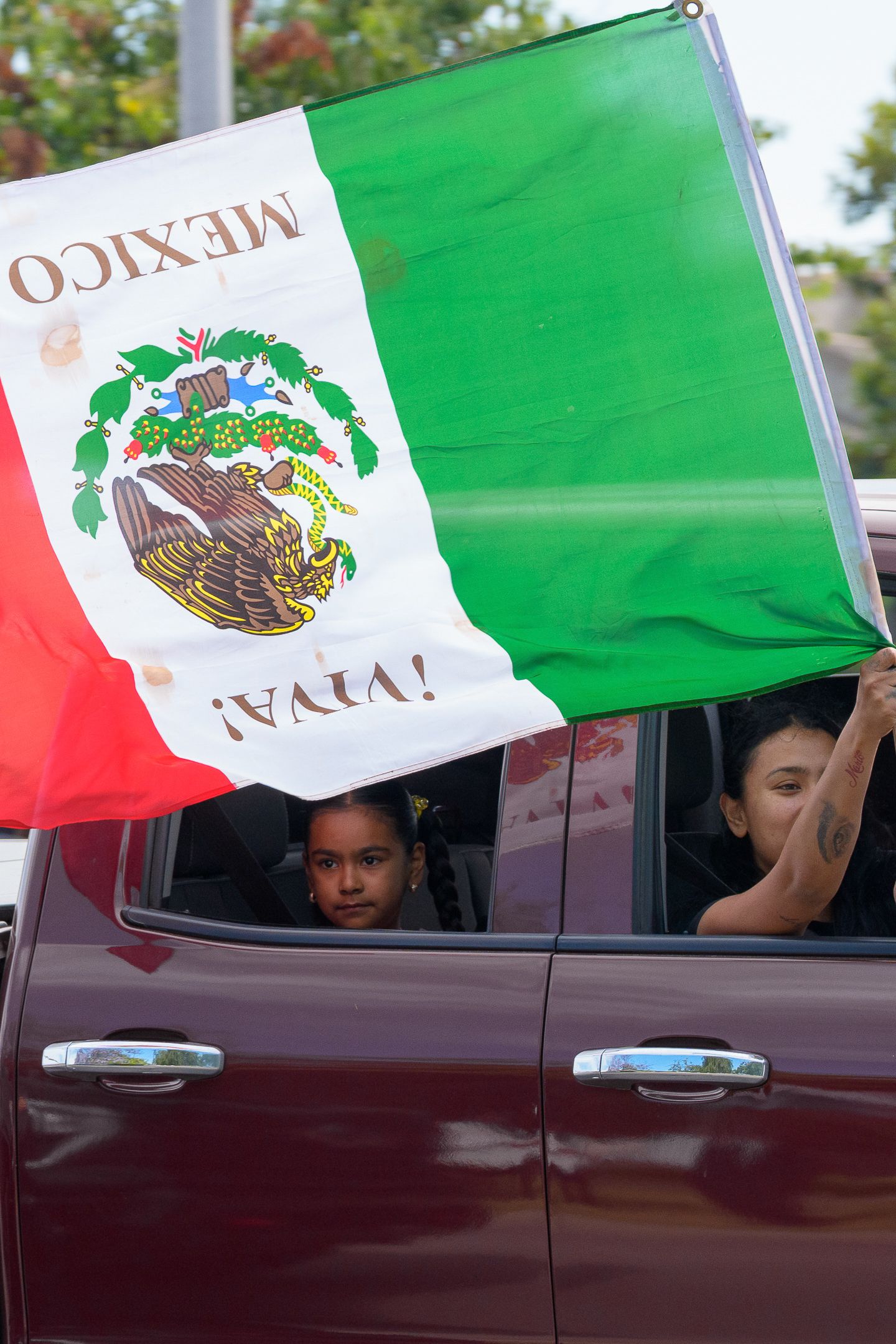 Mexican flags wave from car windows during a street protest or parade.
