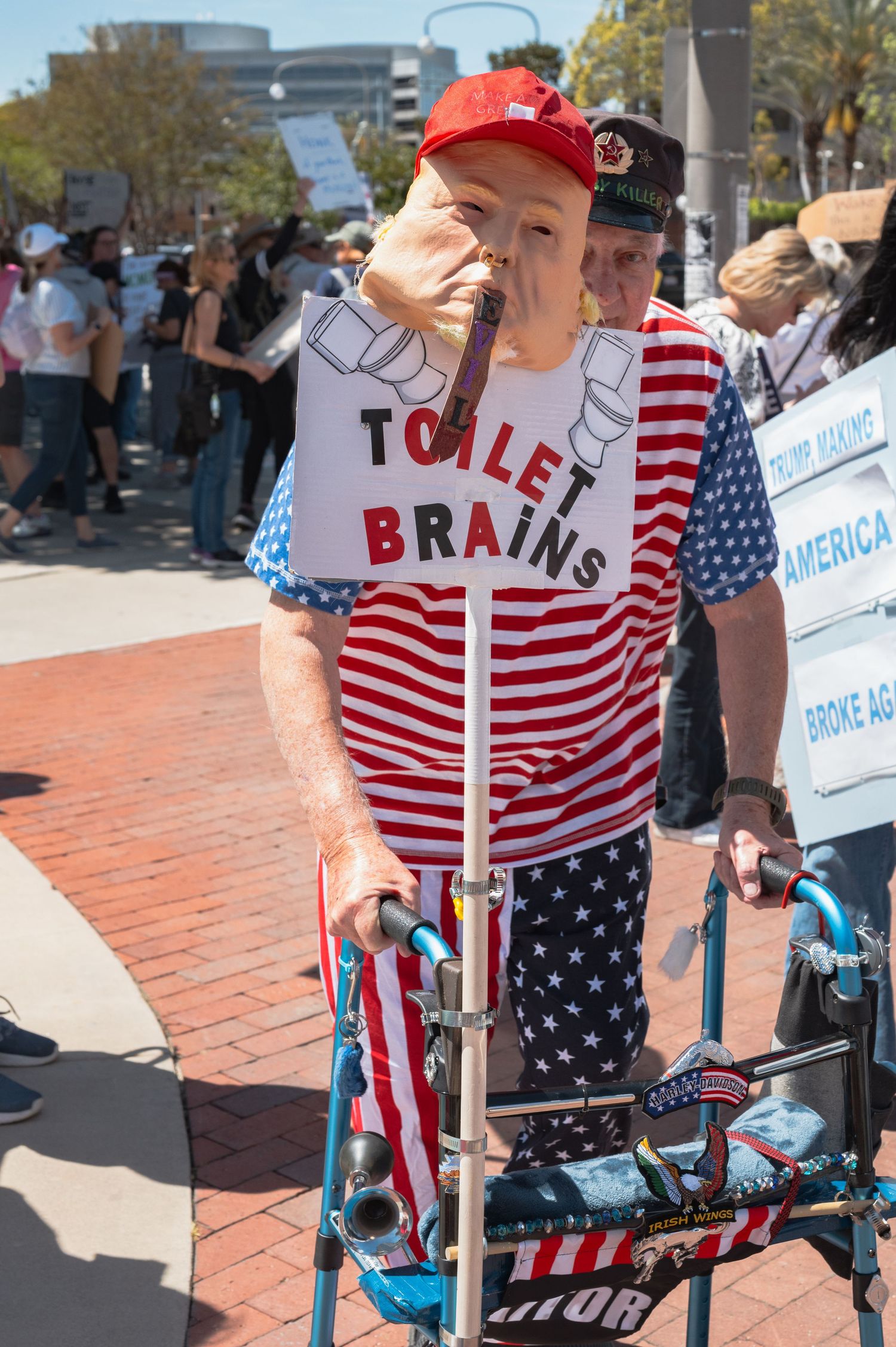 People in patriotic clothing holding protest signs on city sidewalk.