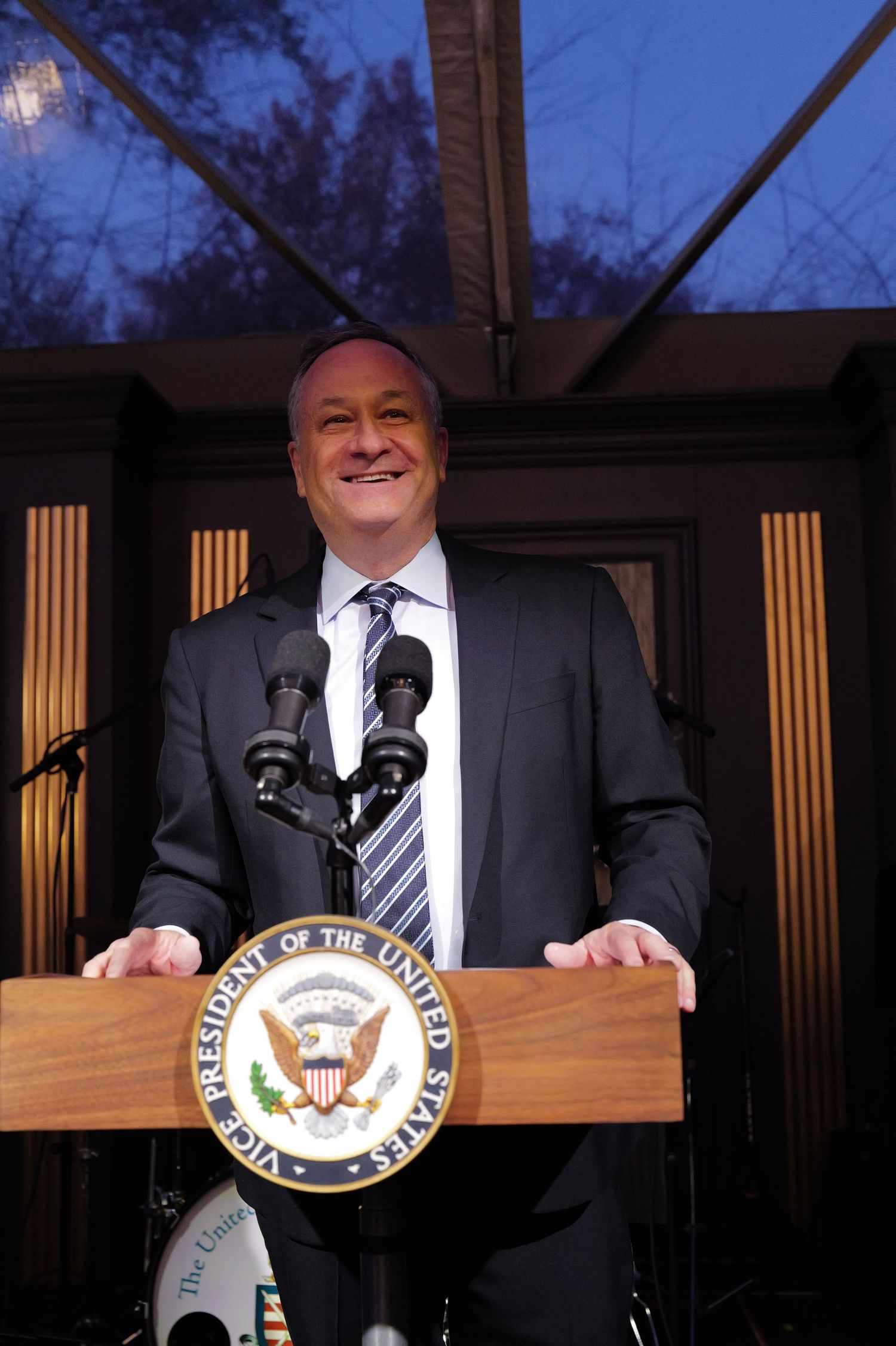 A speaker stands at a wooden podium with the Vice Presidential seal during an evening outdoor address.