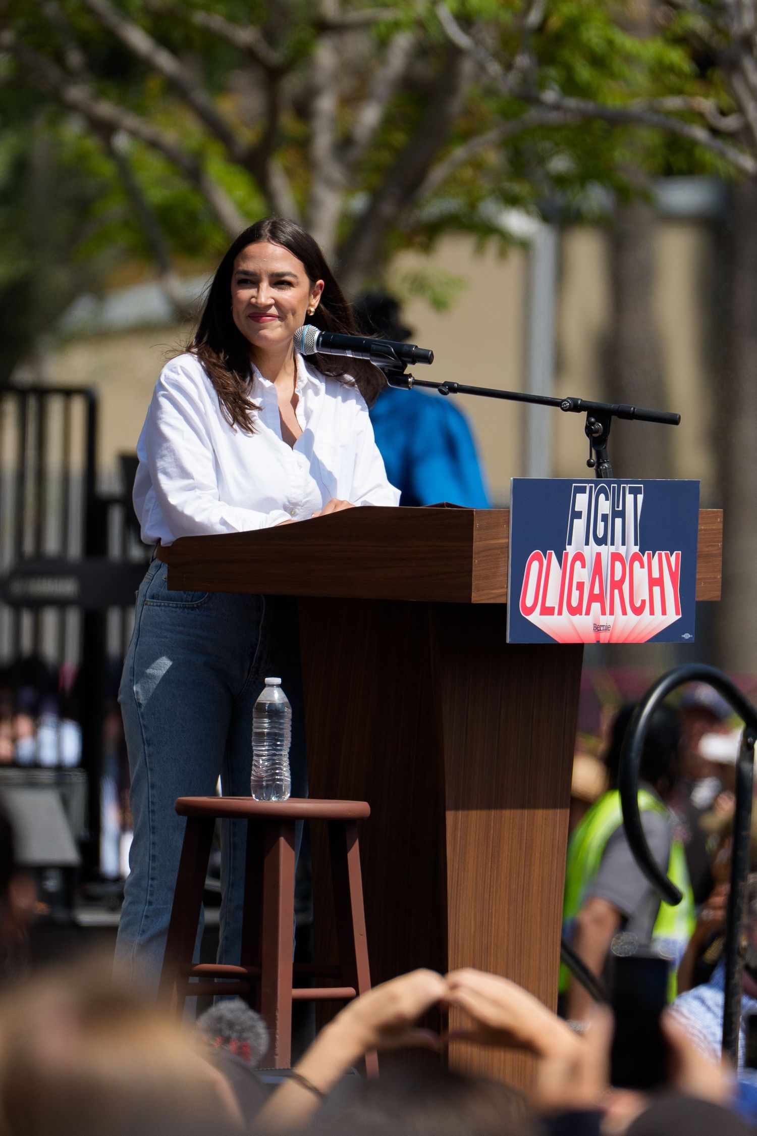 A wooden podium with signs reading 'Fight Oligarchy' at an outdoor political event.