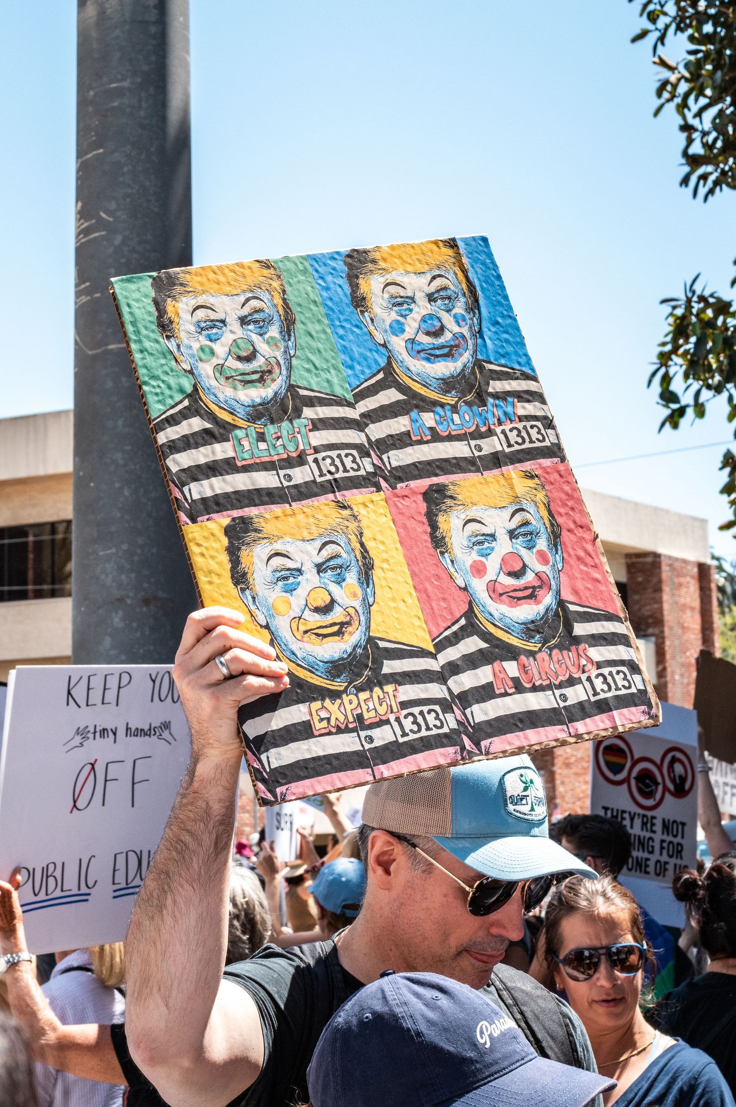 Protesters holding colorful artistic signs at outdoor demonstration.