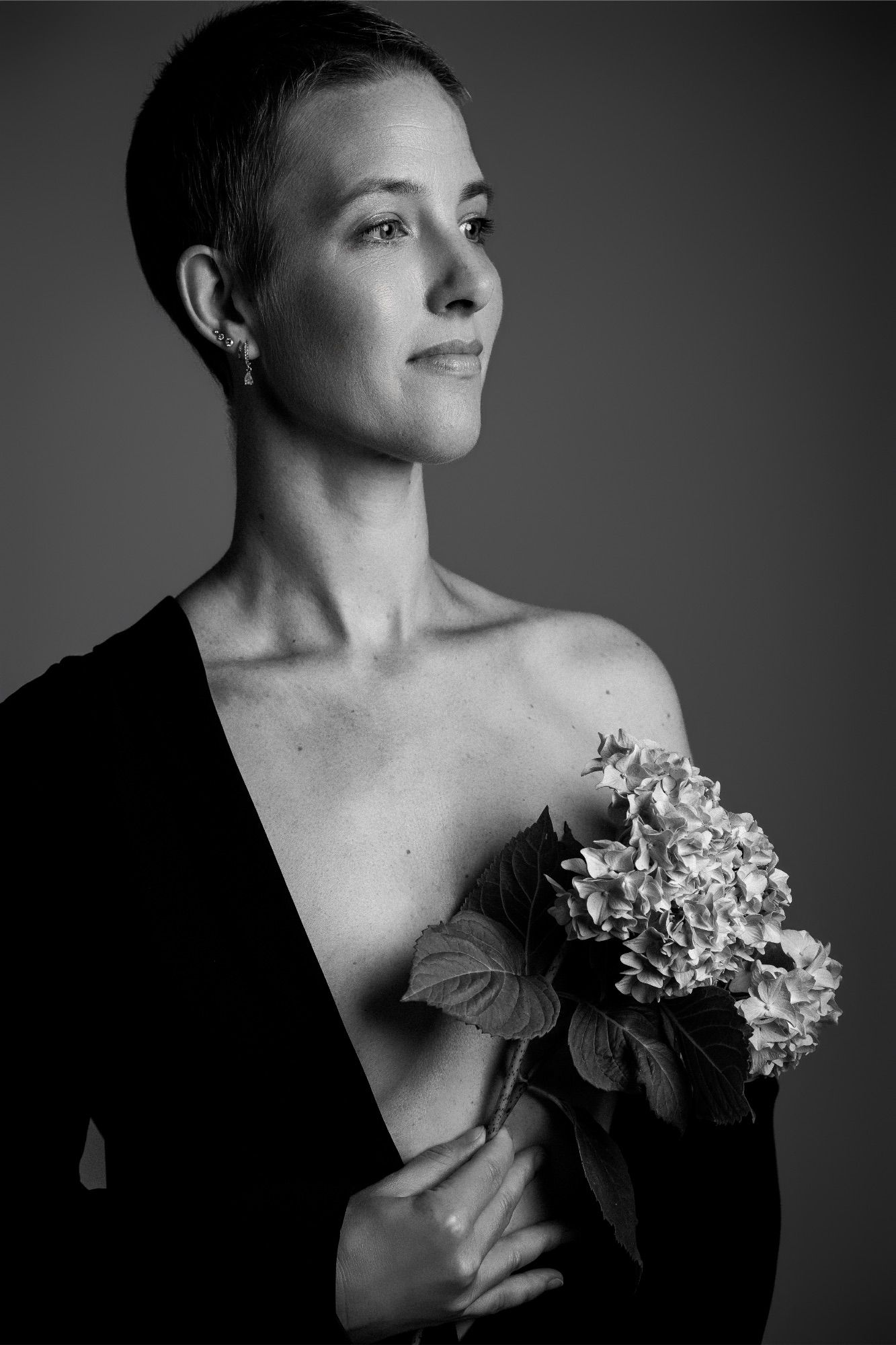 Black and white portrait of a woman with short hair holding hydrangea flowers, wearing an off-shoulder black top.