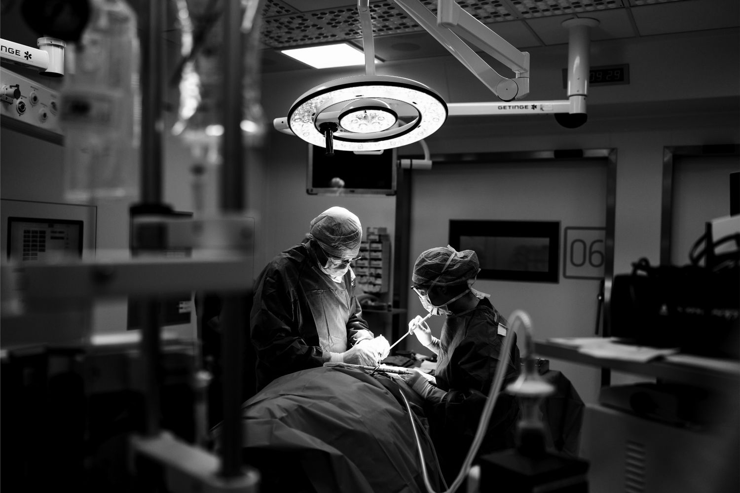 Black and white photo of two surgeons performing an operation under bright overhead lights in a modern operating room.