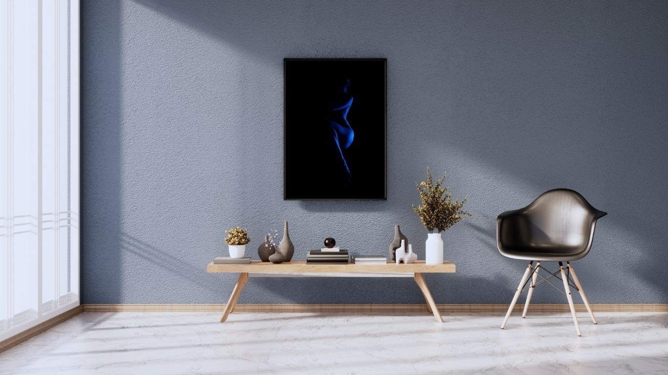 Modern living room with gray walls featuring abstract blue smoke art print above a wooden bench with decor and a black chair.