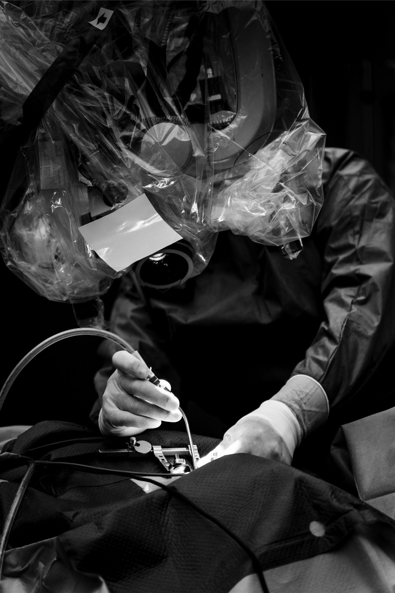 Dramatic black and white portrait of surgeon in the OR behind a microscope performing an operation. Medical documentary by Constanze Ariane.